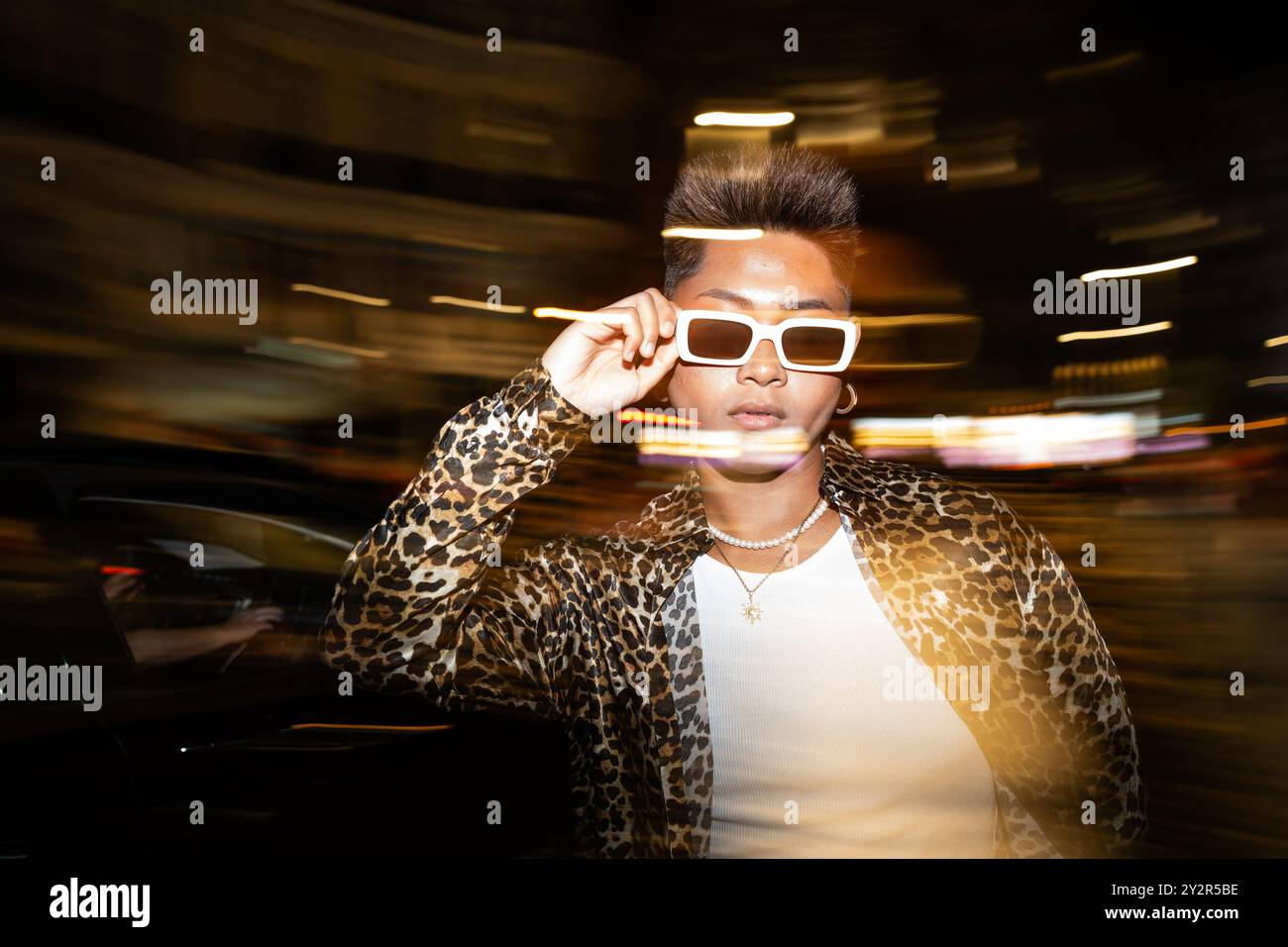 Porträt modischer, nicht-binärer Einzelpositionen in urbaner Nachtszene mit dynamischer Bewegungsunschärfe und lebendigen Lichtspuren. Stockfoto