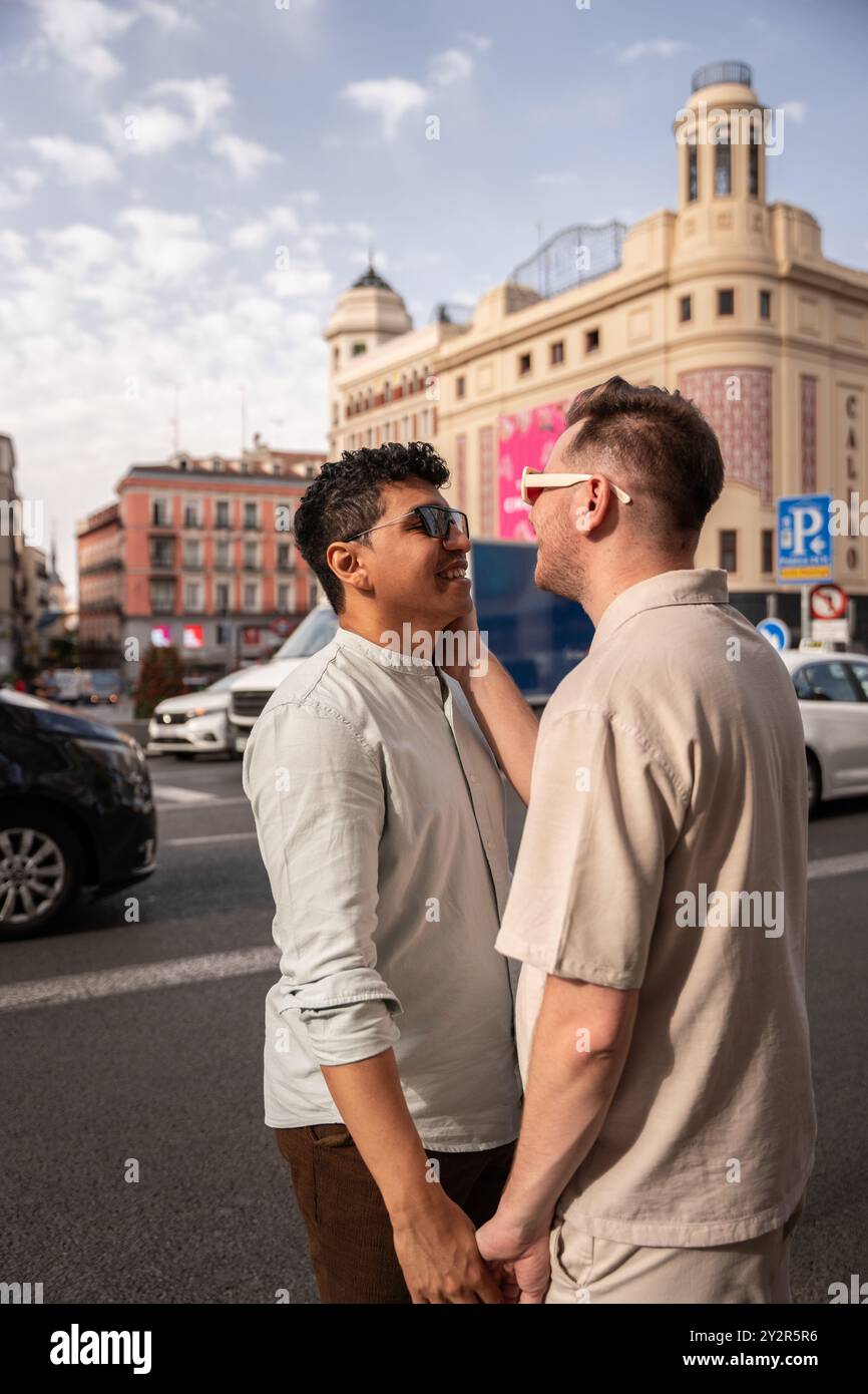 In einem Moment der Zärtlichkeit fesselt dieses multiethnische schwule Paar ein Lächeln auf einer belebten Straße der Stadt und hebt Liebe und Verbundenheit hervor Stockfoto