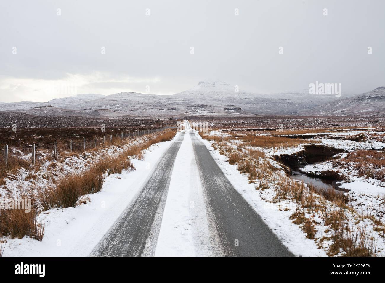 Eine schneebedeckte Straße zieht sich durch das verlassene Gelände der schottischen Highlands, wobei die raue Landschaft durch die raue Landschaft stürzt. Ideal zur Darstellung von Wint Stockfoto