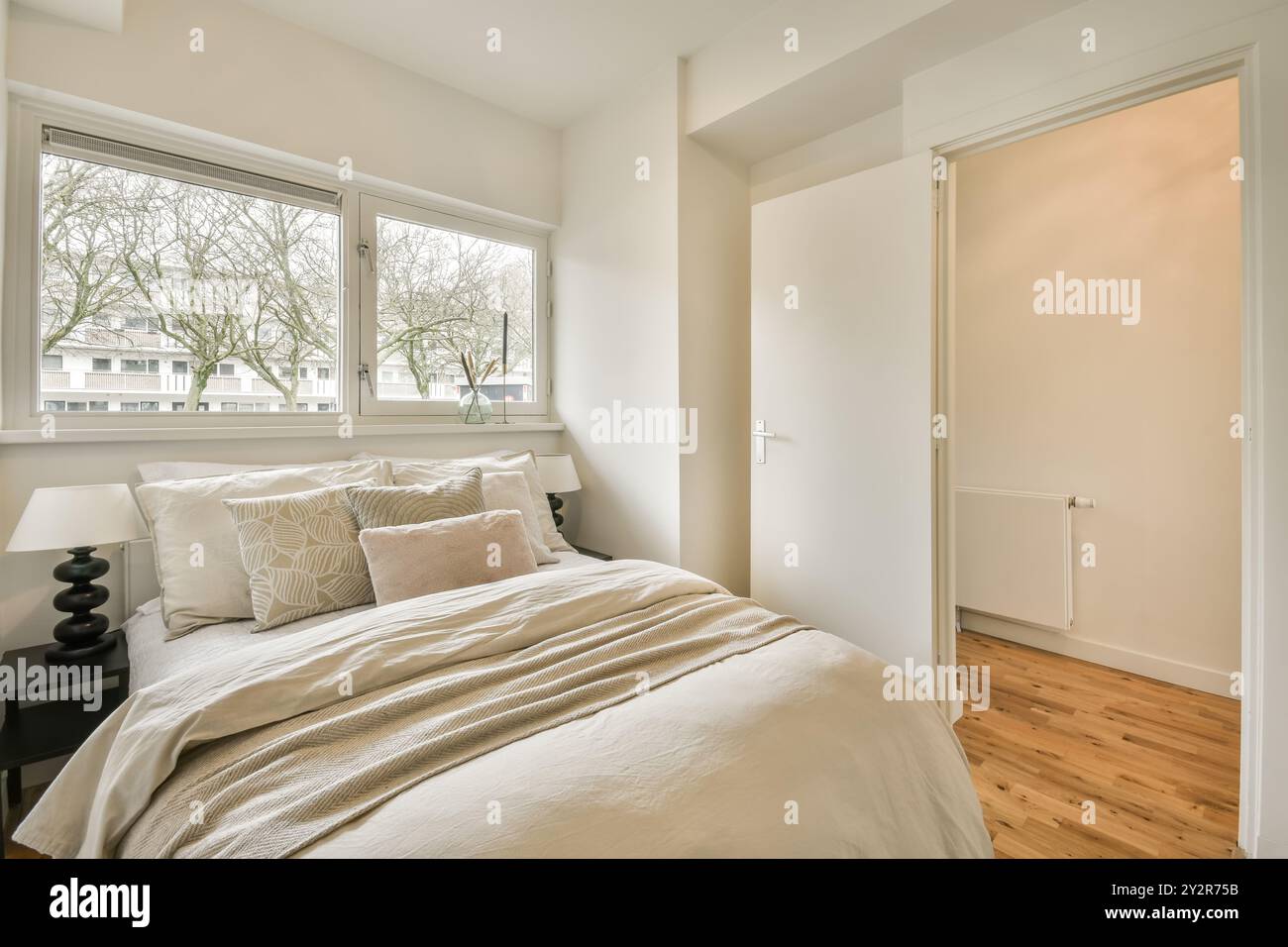 Ein ruhiges Schlafzimmer mit einem komfortablen Bett mit weichen Kissen, großen Fenstern für Tageslicht und einer einfachen, eleganten Einrichtung. Stockfoto
