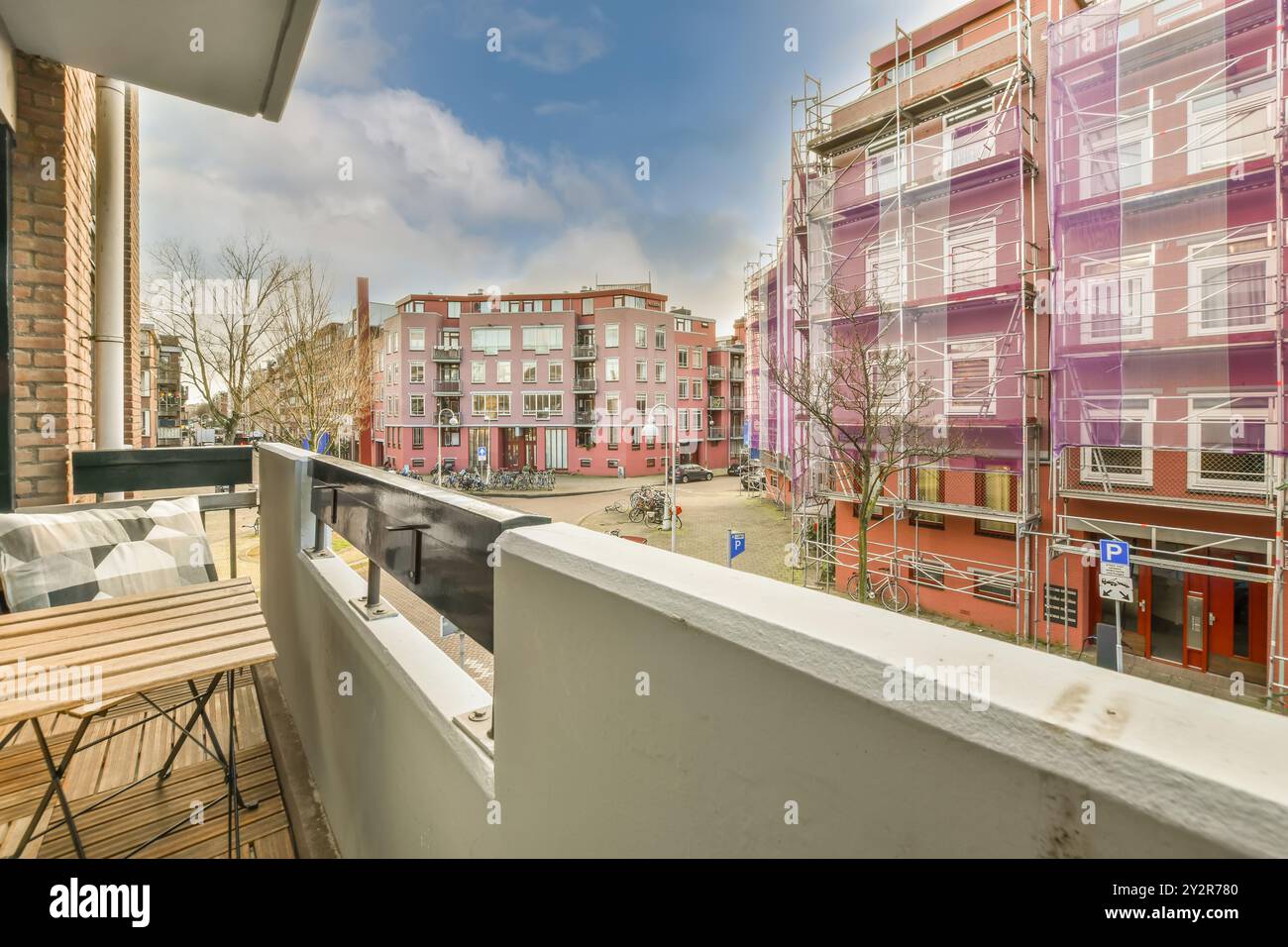 Heller und einladender Stadtbalkon mit Holztisch und farbenfroher Stadtlandschaft unter klarem blauem Himmel. Stockfoto