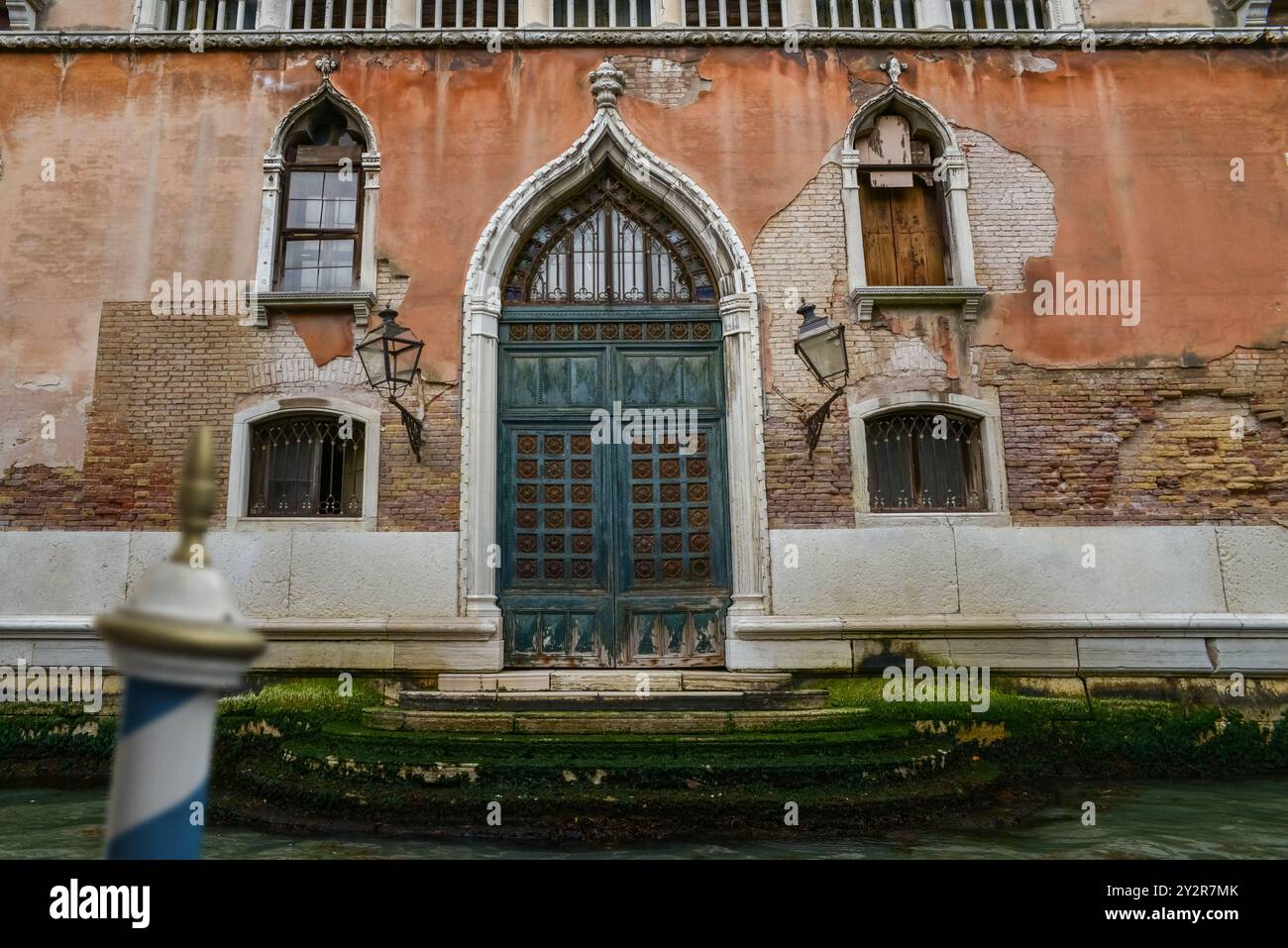 Erfassen Sie ein altes venezianisches Gebäude mit detaillierten Mauerwerken, gotischen Fenstern und einer großen Tür, die das architektonische Erbe Venedigs widerspiegelt Stockfoto