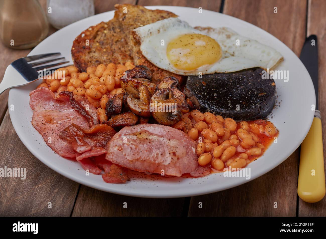 Warmes Frühstück mit Schwarzpudding, Speck, Pilzen, Bohnen, gebratenem Brot und Spiegelei. Stockfoto