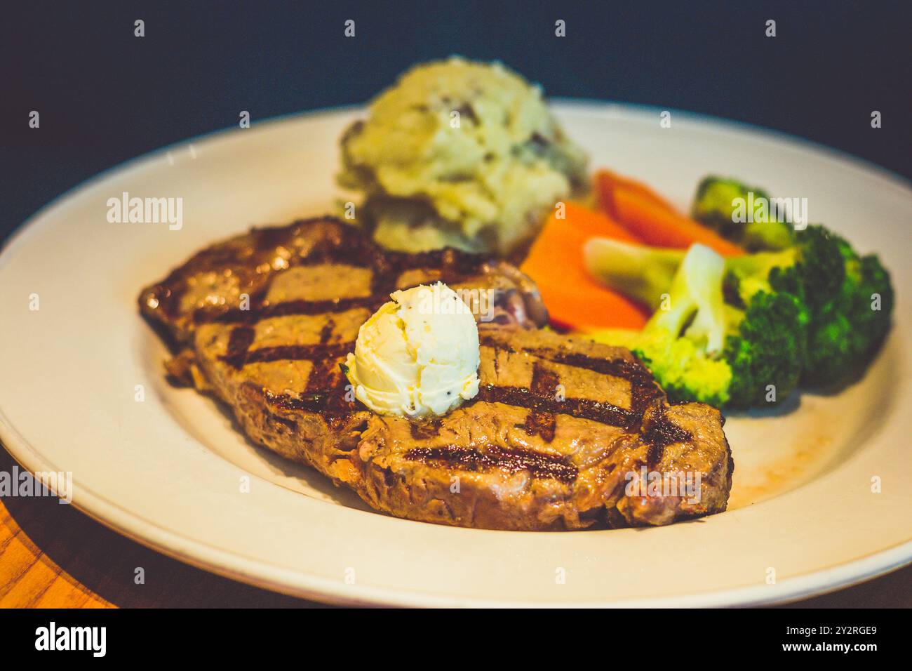340 g New York Strip Steak, gegrillt und mit Kräuterbutter belegt. Serviert mit goldenem Kartoffelpüree und frischem Gemüse Stockfoto