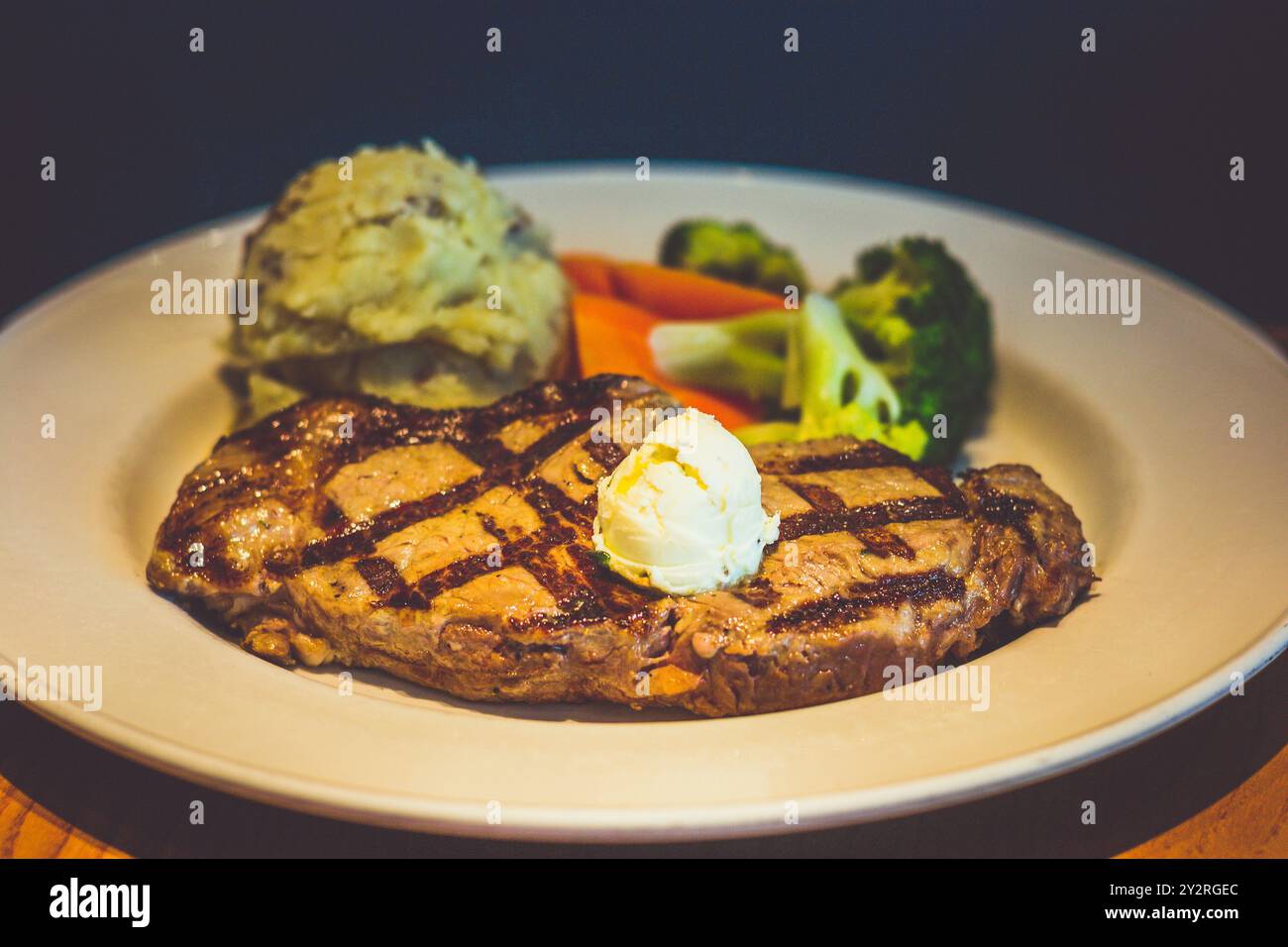 340 g New York Strip Steak, gegrillt und mit Kräuterbutter belegt. Serviert mit goldenem Kartoffelpüree und frischem Gemüse Stockfoto