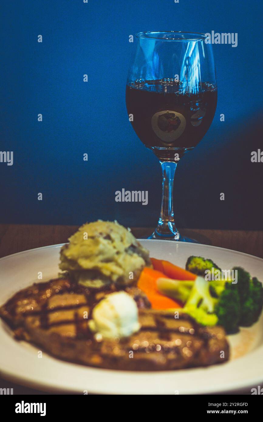 340 g New York Strip Steak, gegrillt und mit Kräuterbutter belegt. Serviert mit goldenem Kartoffelpüree und frischem Gemüse Stockfoto