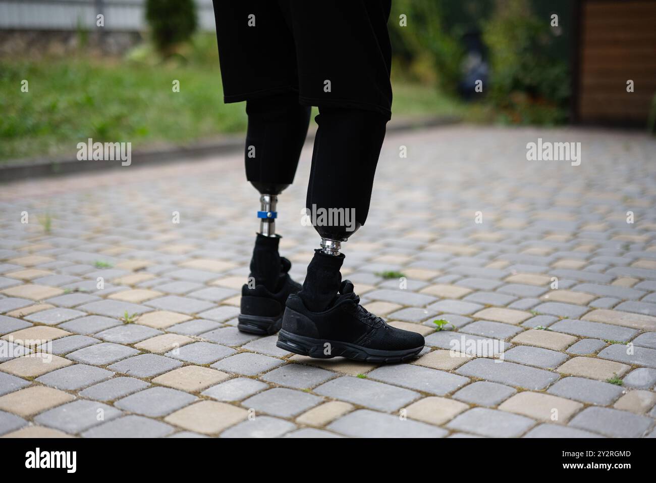 Ein Nahbild einer Person mit Prothesenbeinen in schwarzen Schuhen, die auf einem Kopfsteinpflasterweg steht. Das Bild vermittelt Stärke, Unabhängigkeit, Stockfoto