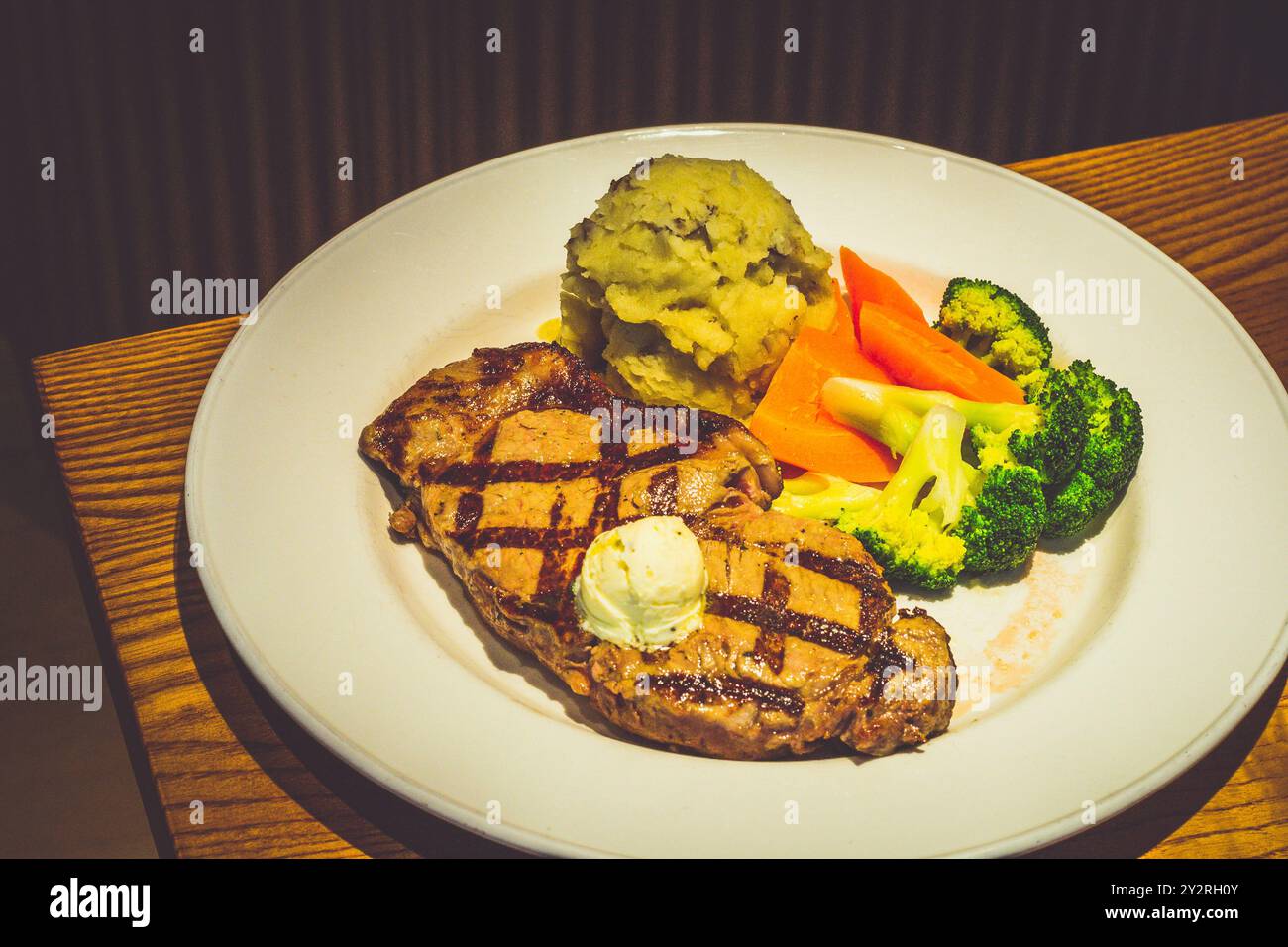 340 g New York Strip Steak, gegrillt und mit Kräuterbutter belegt. Serviert mit goldenem Kartoffelpüree und frischem Gemüse Stockfoto