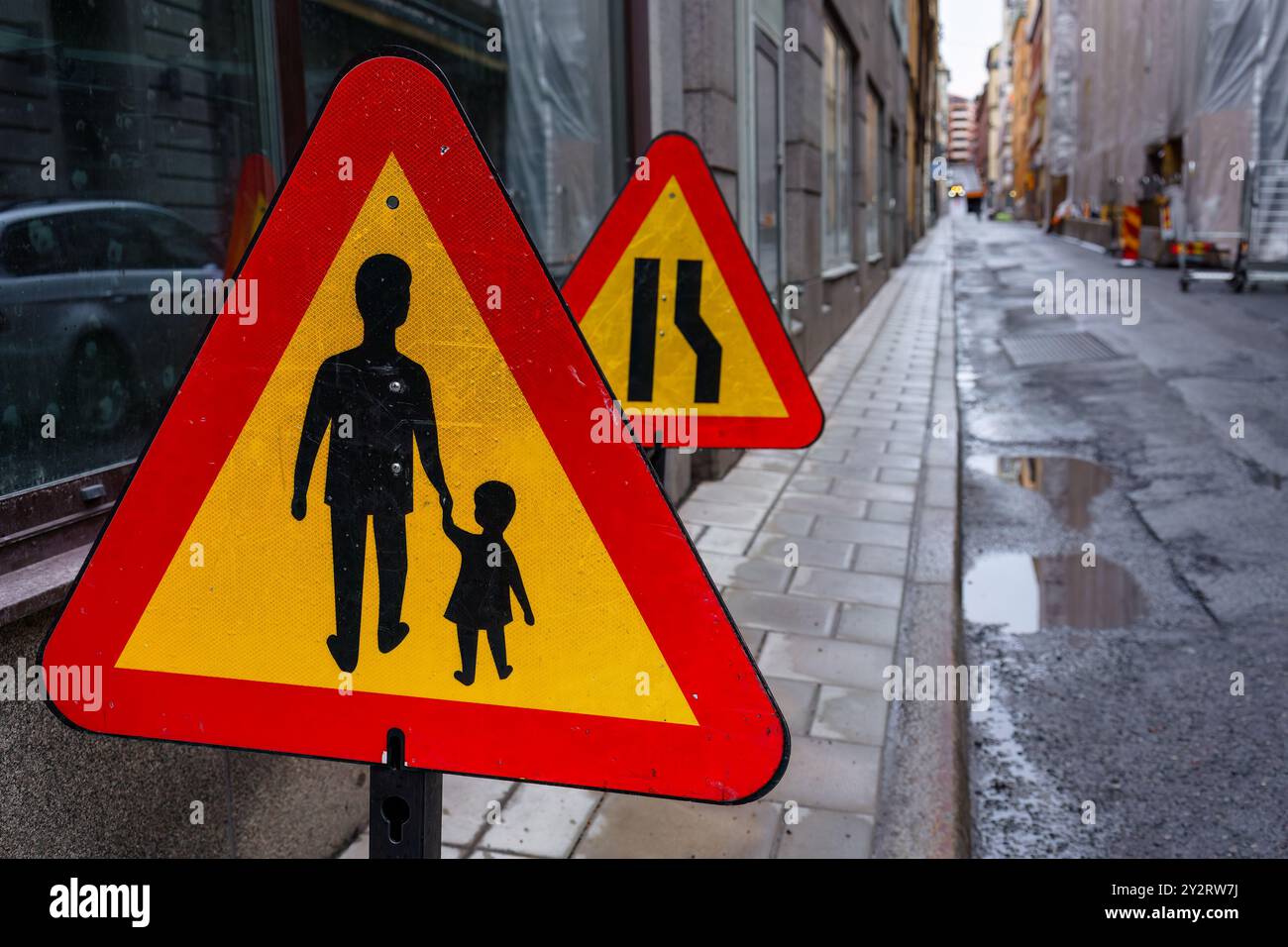 Ein gelbes und rotes Fußgängerwarnschild auf einer Stadtstraße Stockfoto