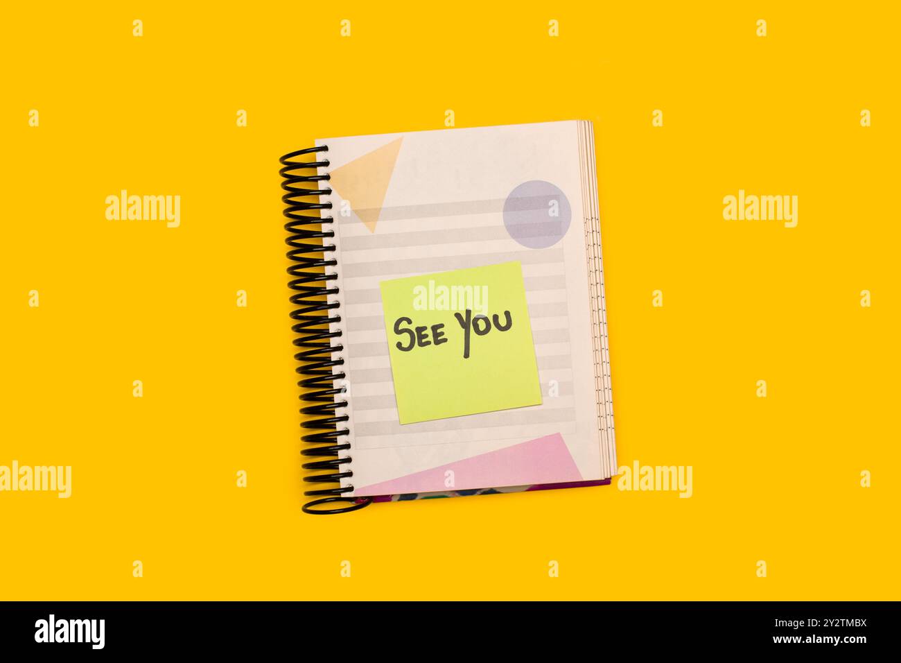 Ein spiralförmiger Notizblock mit einem klebrigen Papier mit handgeschriebenem „See You“-Satz auf gelbem Hintergrund Stockfoto