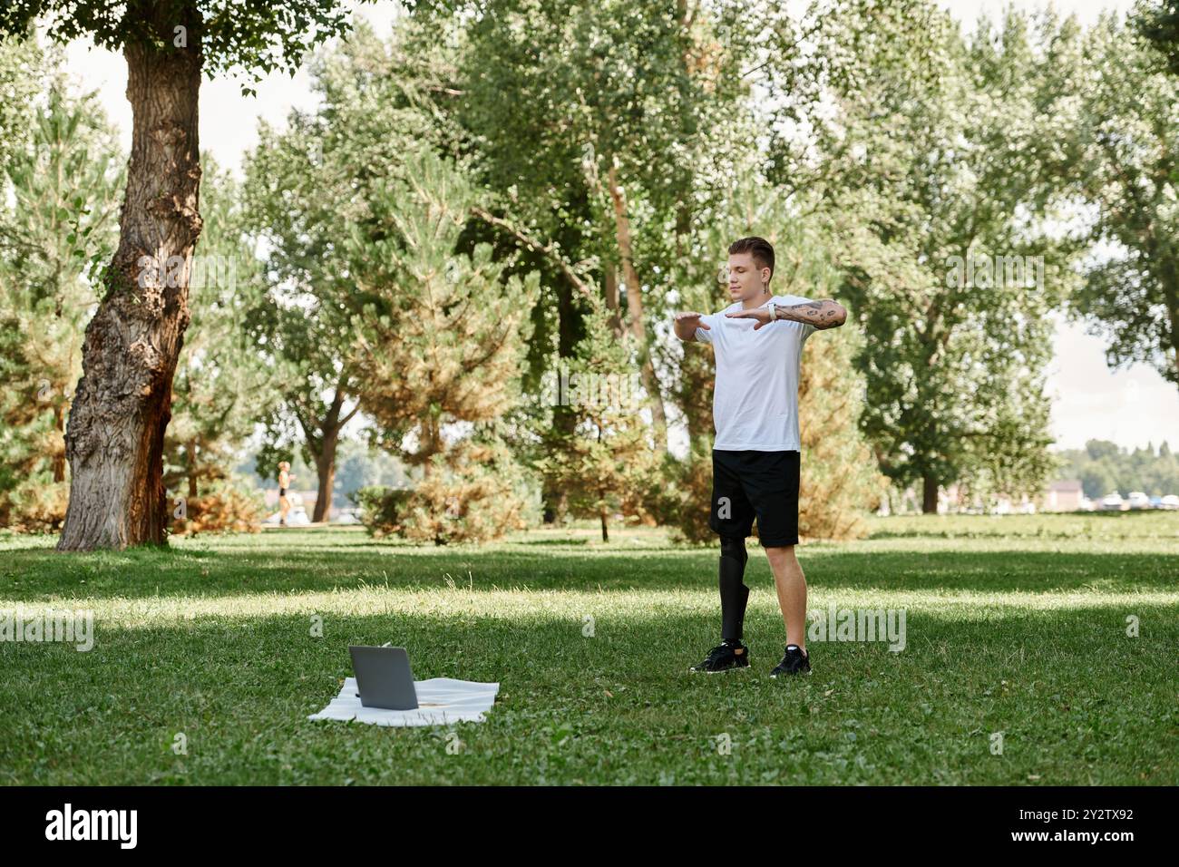 Tätowierter junger Mann trainiert in einem Park und nimmt mit Entschlossenheit an einer Online-Fitnessstunde Teil. Stockfoto
