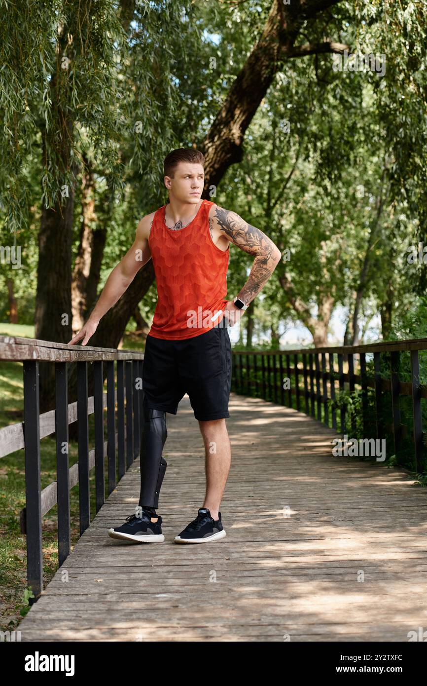 Ein junger Mann mit künstlichem Bein, der auf einer Brücke steht, umgeben von Bäumen im Park Stockfoto