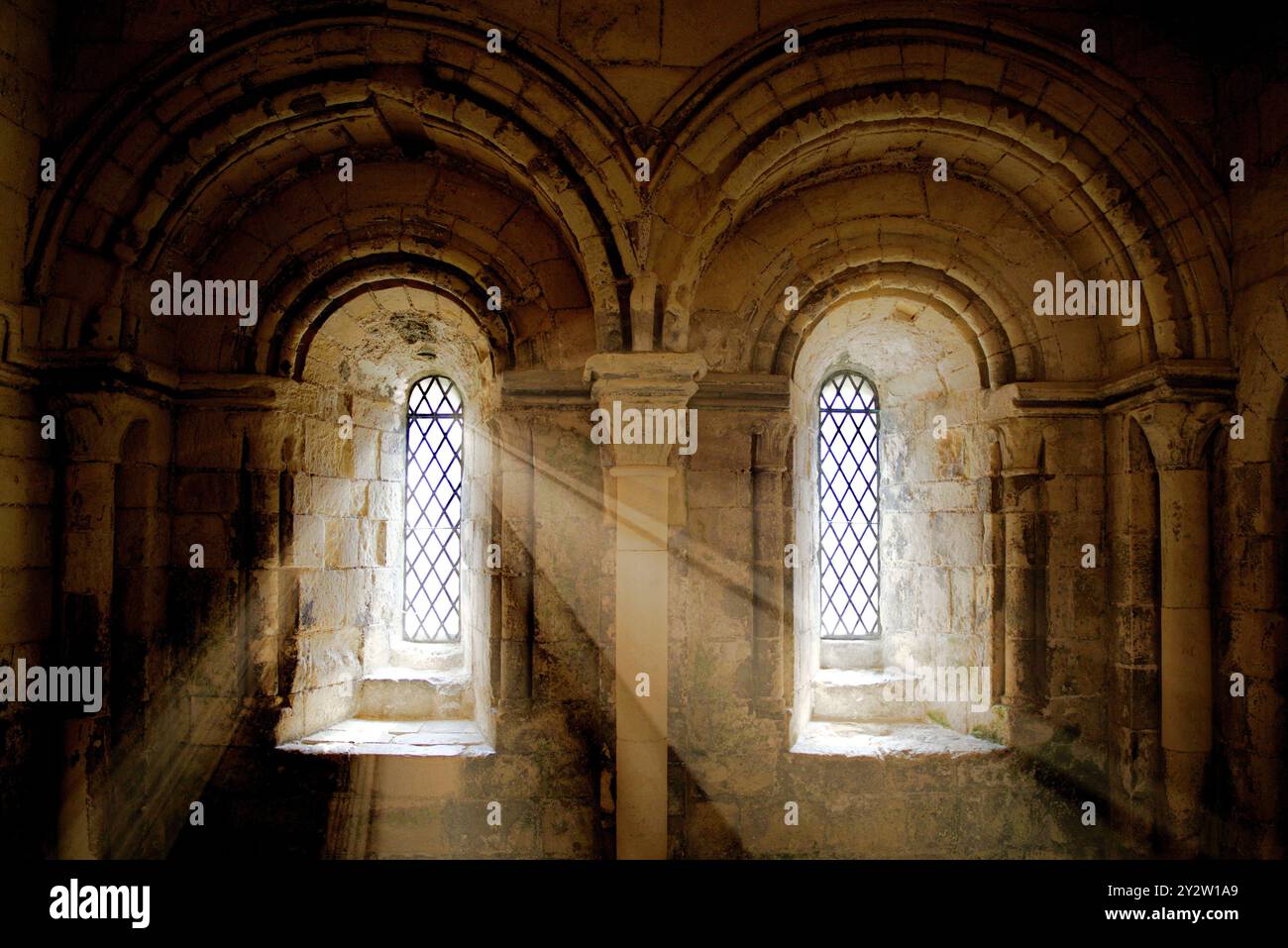 Sonnenlicht strömt durch zwei Bogenfenster in einem alten Steingebäude und schafft eine ruhige und historische Atmosphäre. Stockfoto