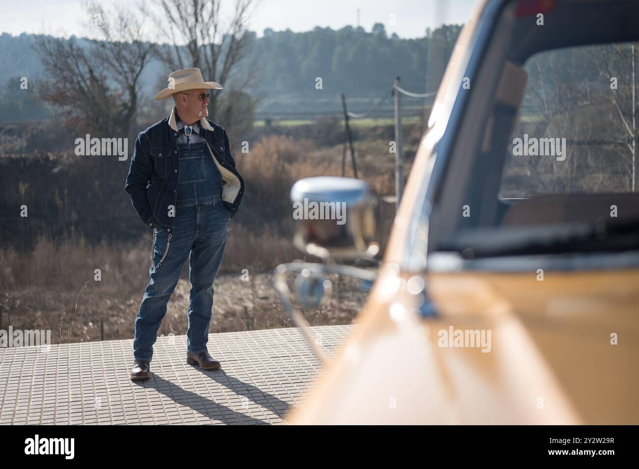 Detail eines typisch amerikanischen Charakters mit Jeans, Lederstiefeln, Sonnenbrille und Strohhut neben seinem klassischen Pickup-Truck Stockfoto