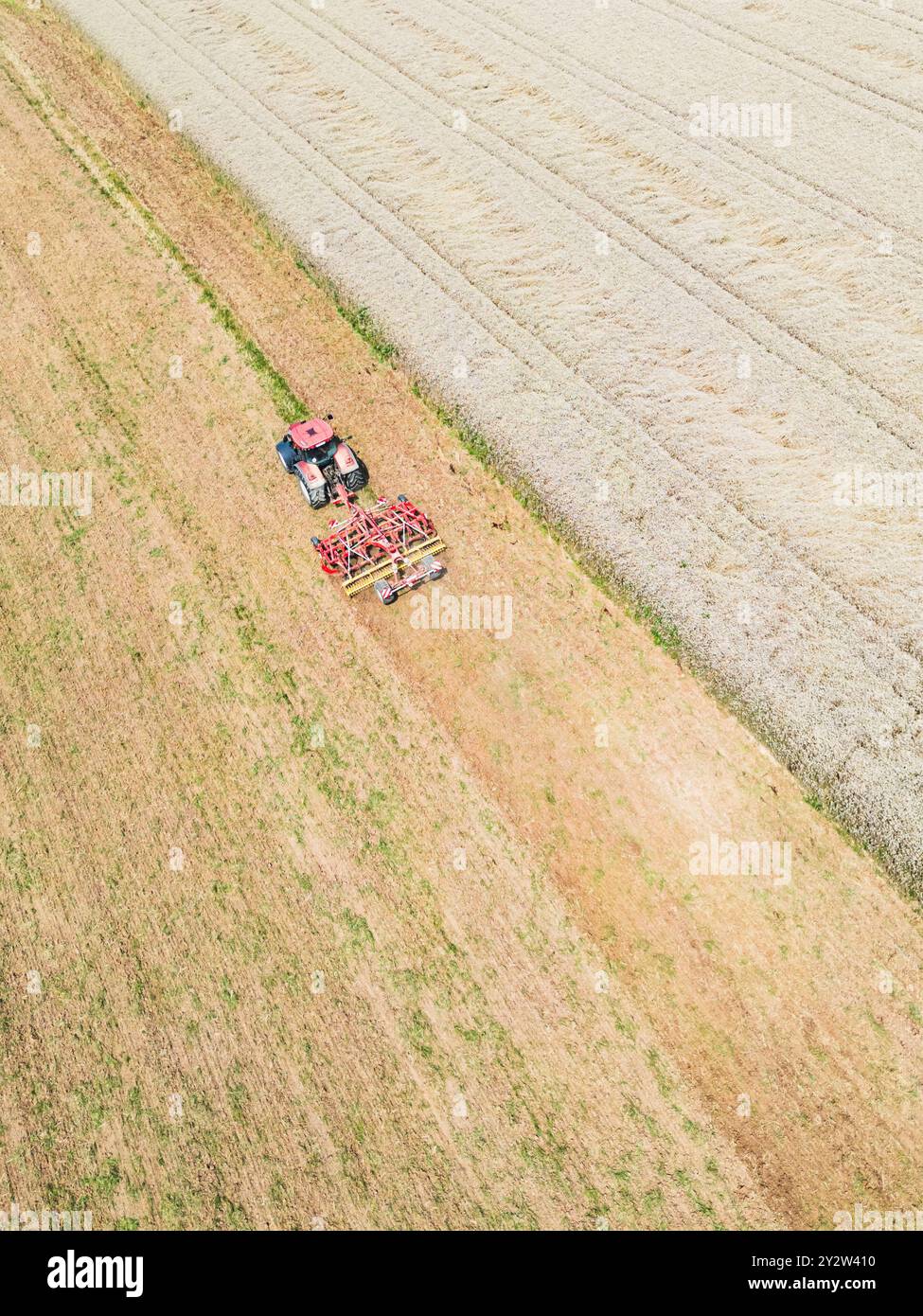 Draufsicht eines roten Traktors, der an einem sonnigen Sommertag das Feld pflügt Stockfoto