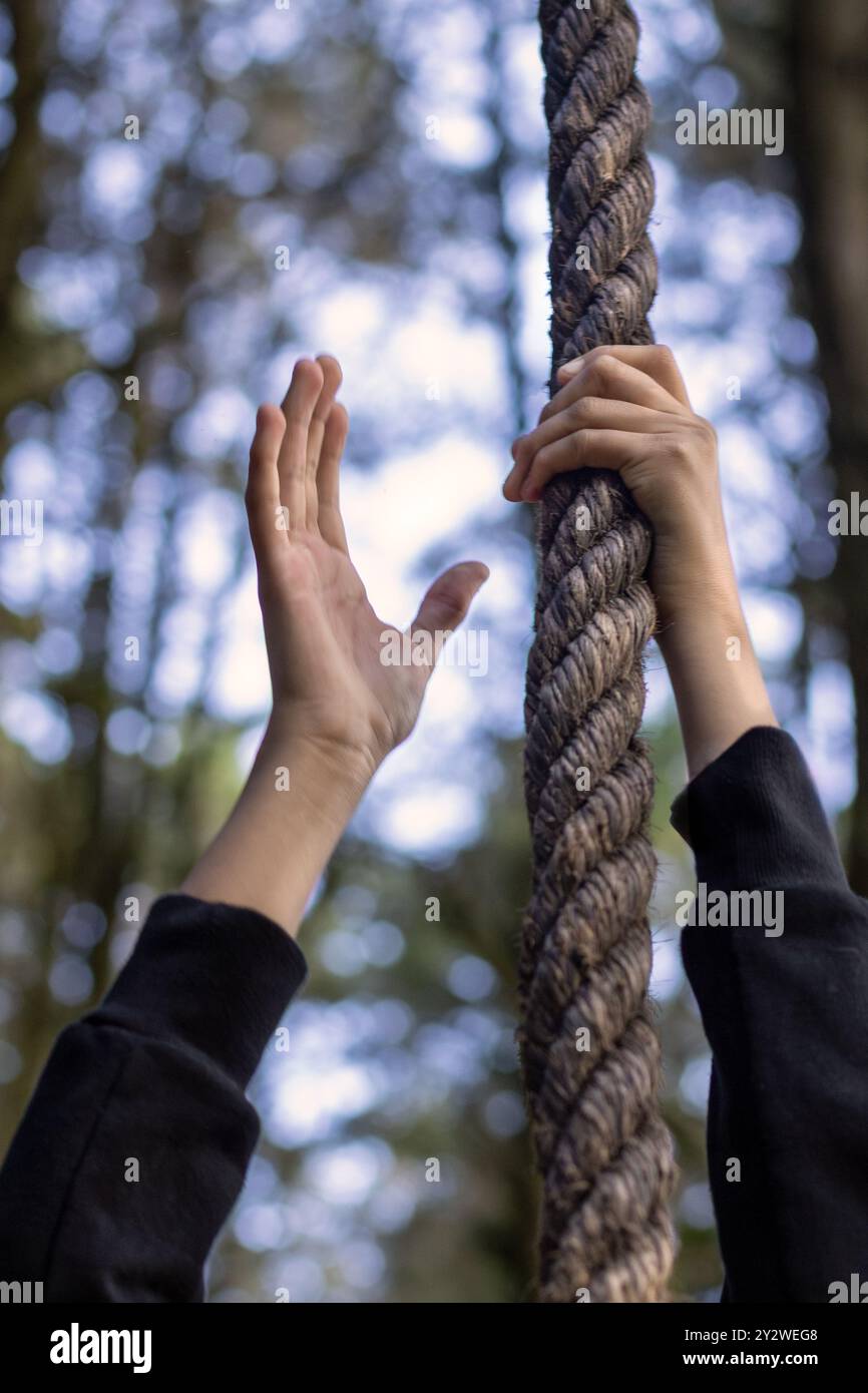 Eine Nahaufnahme der Hände, die ein dickes Seil mit einem verschwommenen Waldhintergrund greifen Stockfoto