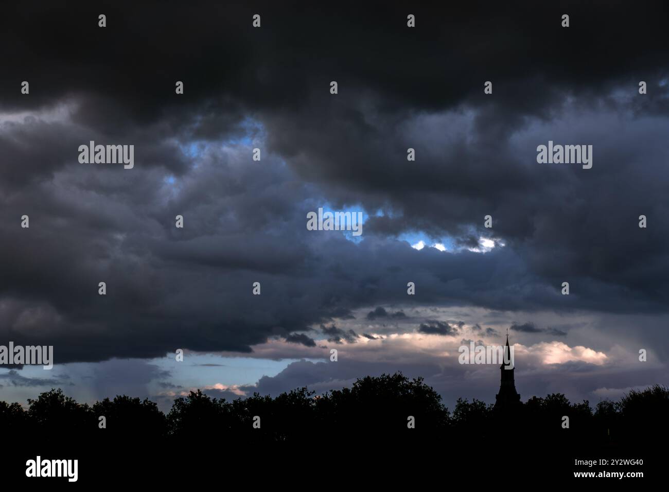 Baumkronen und Kirchturm, die vor schwarzer Nimbostratus-Wolke gehalten werden und im Spätsommer Regen bringen Stockfoto