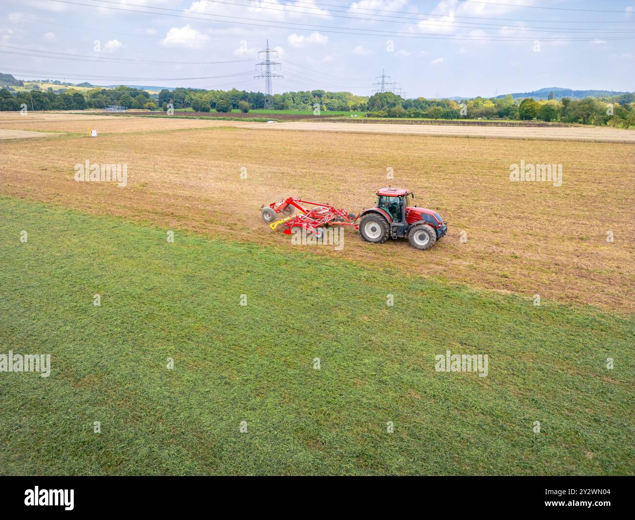 Seitenansicht eines roten Traktors, der an einem sonnigen Sommertag das Feld pflügt Stockfoto