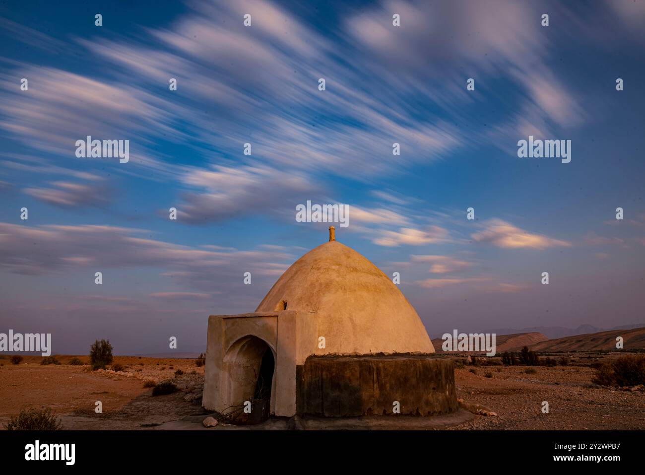 Eine ruhige Wüstenlandschaft mit einer kleinen Kuppelstruktur unter einem dynamischen, wolkenbedeckten Himmel Stockfoto Eine ruhige Wüstenlandschaft mit einer kleinen Kuppelstruktur unter einem dynamischen, wolkenbedeckten Himmel Stockfoto