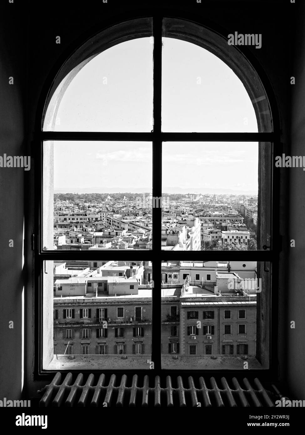 Ein Schwarzweißfoto der Stadt Rom, das durch ein altes Fenster hoch oben im Petersdom gesehen wird Stockfoto