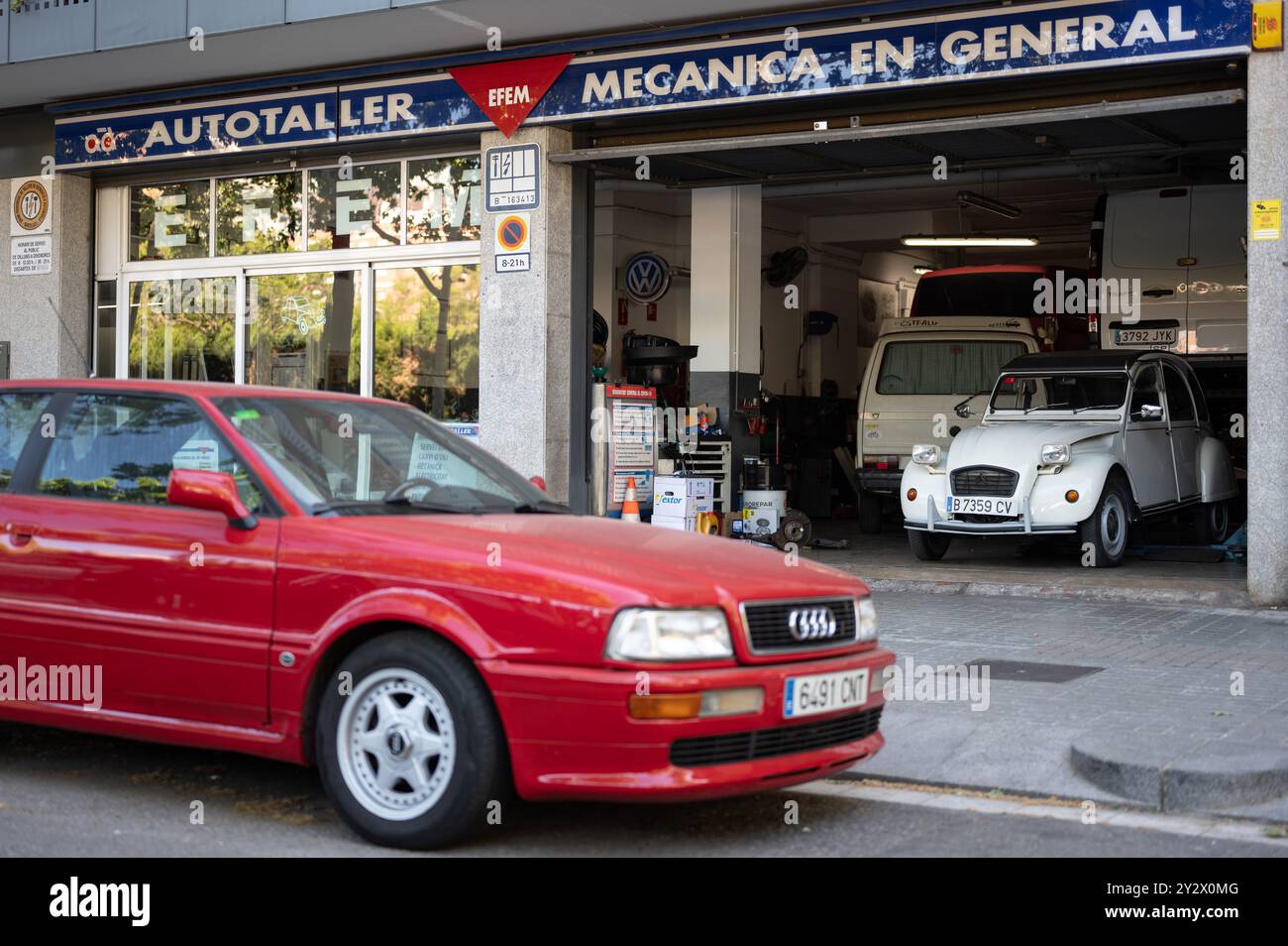 Ein Mechaniker aus einer Werkstatt in Barcelona. Im Inneren befindet sich ein alter, klassischer weißer Citroen 2cv und draußen ein schönes rotes Audi Coupé Stockfoto