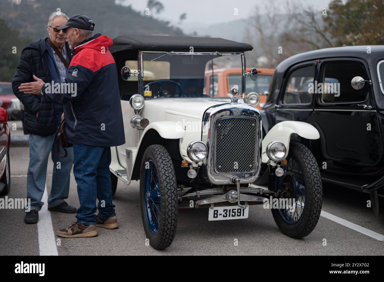 Vorderansicht eines historischen Sammlerwagens, eines weißen Austin Seven mit schwarzem Softtop. Der Besitzer spricht mit einem Freund nebenan Stockfoto