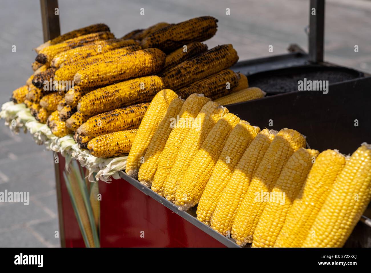 Frisch gegrillter Mais auf dem Cob, ordentlich in einem belebten Straßenverkäuferstand angeordnet, bietet Passanten einen köstlichen Snack Stockfoto