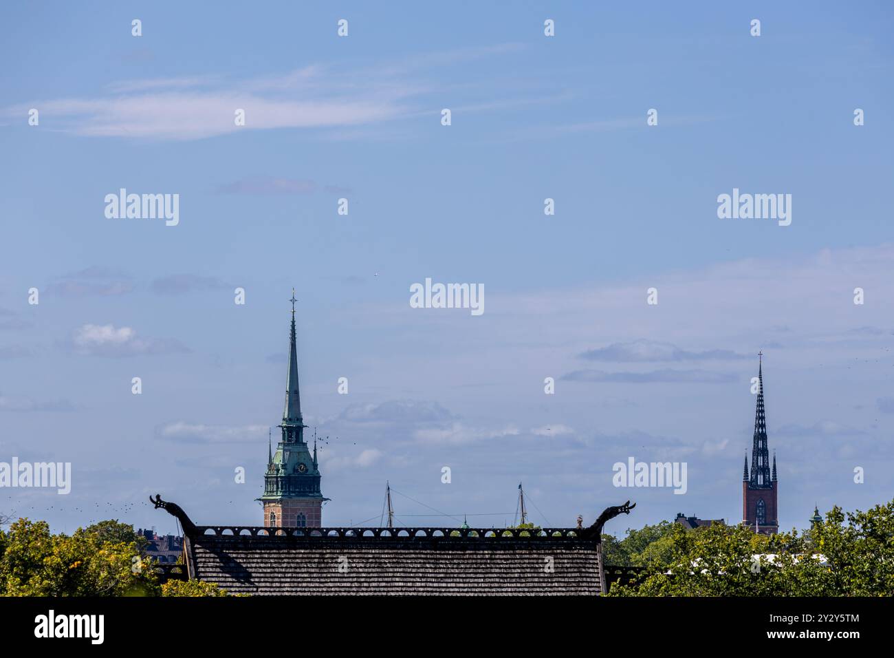 Ein malerischer Blick auf eine Skyline der Stadt mit zwei markanten Kirchtürmen vor einem klaren blauen Himmel. Im Vordergrund befindet sich ein traditionelles Dach mit Dekora Stockfoto
