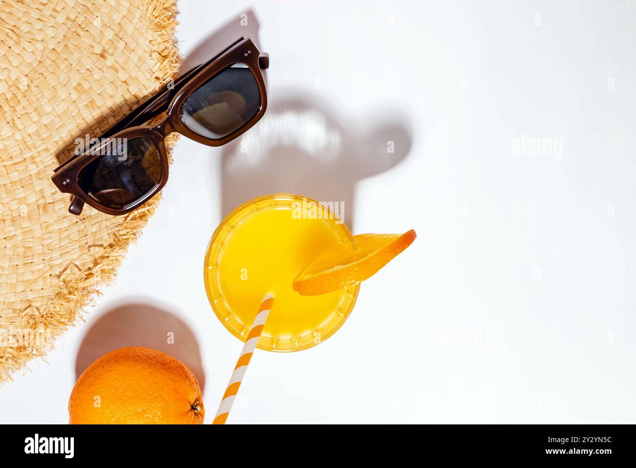 Sommerflachliege mit Strohhut, Orangensaft und Sonnenbrille an einem Sommernachmittag auf einer sonnendurchfluteten Oberfläche Stockfoto