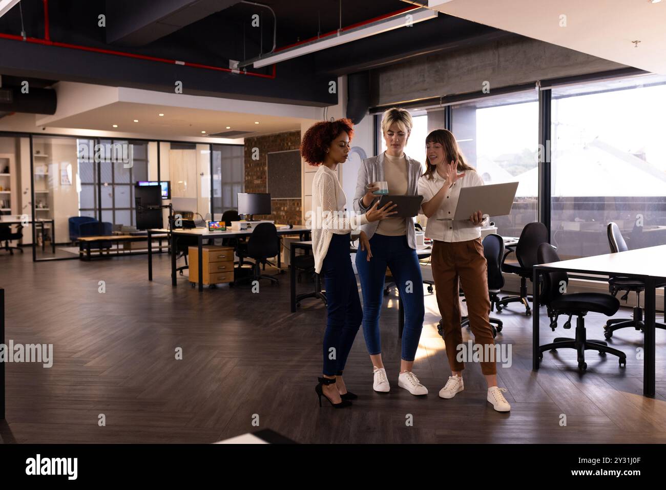 In modernen Büros diskutieren drei Frauen mit verschiedenen Rassen über die Arbeit mit Laptops und Tablets Stockfoto