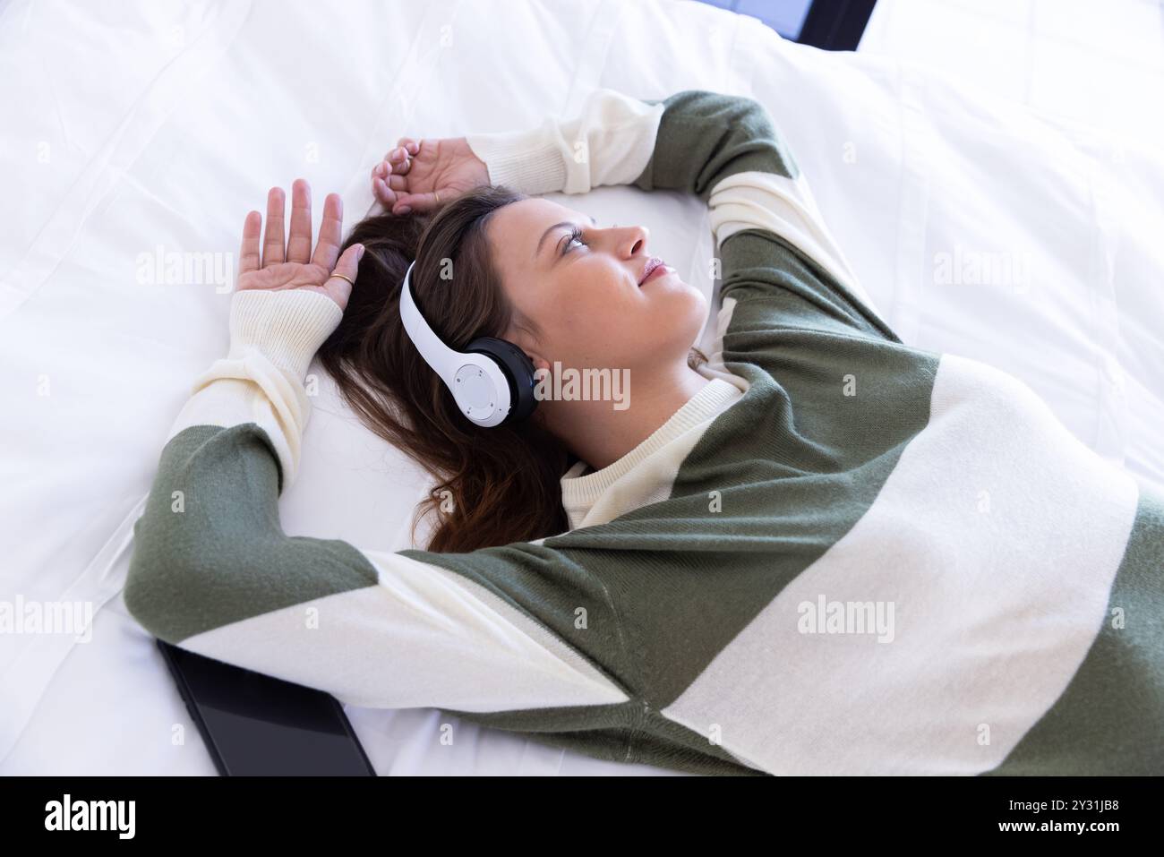 Zu Hause, entspannend auf dem Bett, Frau hört Musik mit Kopfhörern, Smartphone in der Nähe Stockfoto