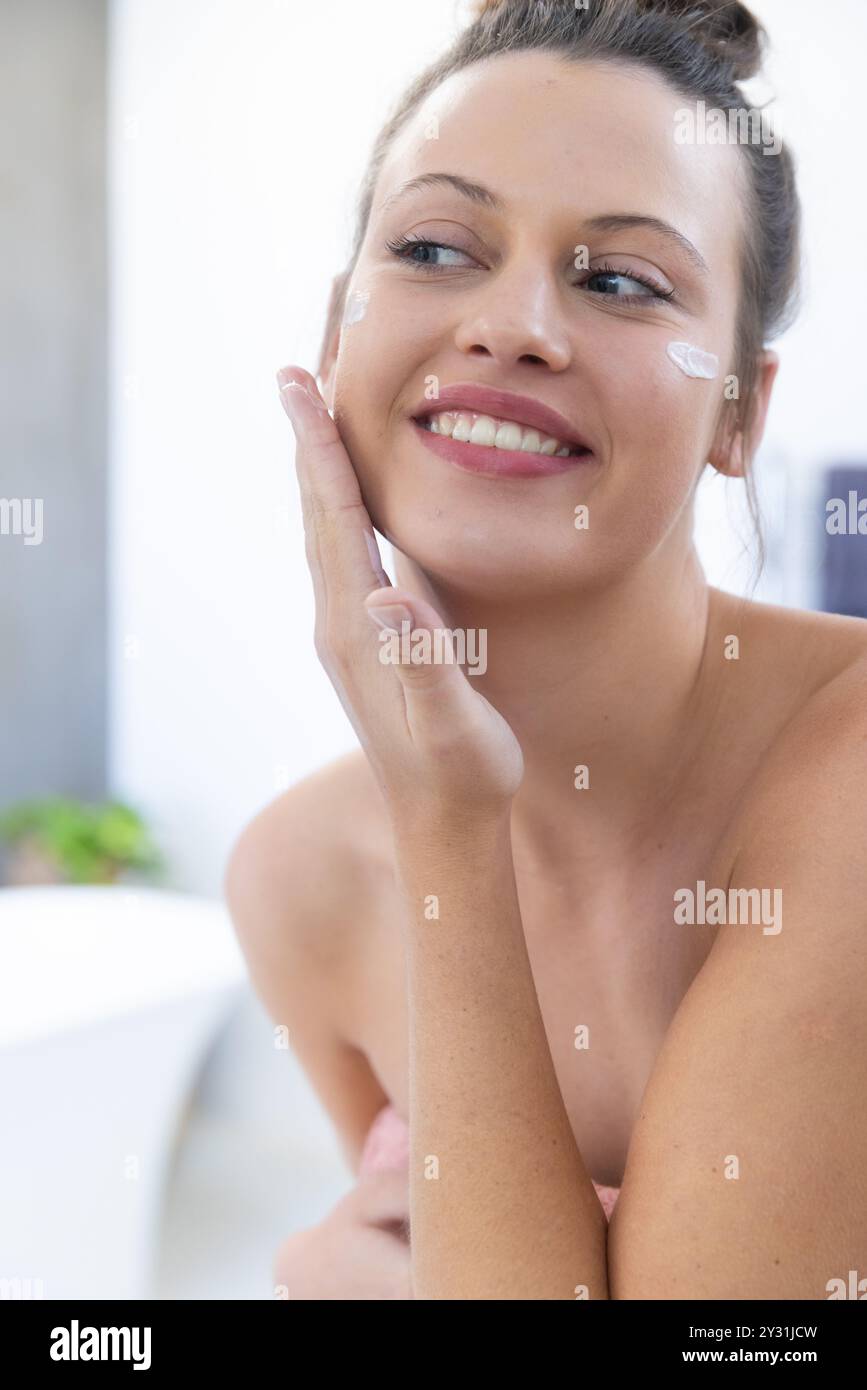 Zu Hause, Gesichtscreme auftragen, junge Frau lächelt und genießt Spa-Behandlungen Stockfoto