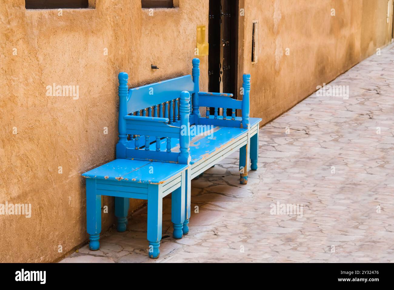 Alte traditionelle blau lackierte Holzbank mit kleinem Tisch in der Straße oder im Innenhof. Holzsofa im Freien im arabischen Stil im Haus. Stockfoto