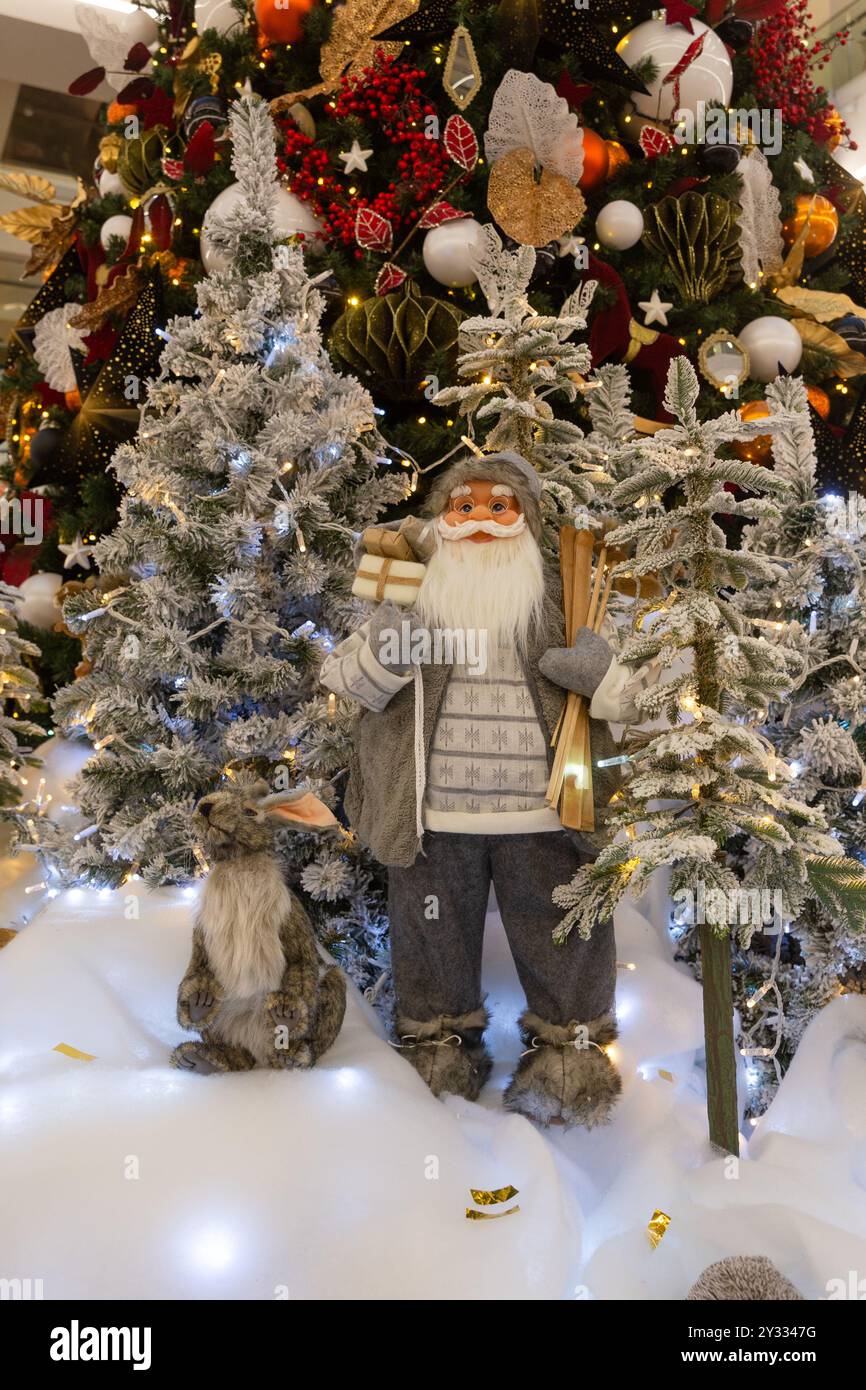 Eine Weihnachtsinstallation mit Weihnachtsmann und Waldtieren am Fuße eines festlich geschmückten Weihnachtsbaums im großen Einkaufszentrum. Stockfoto