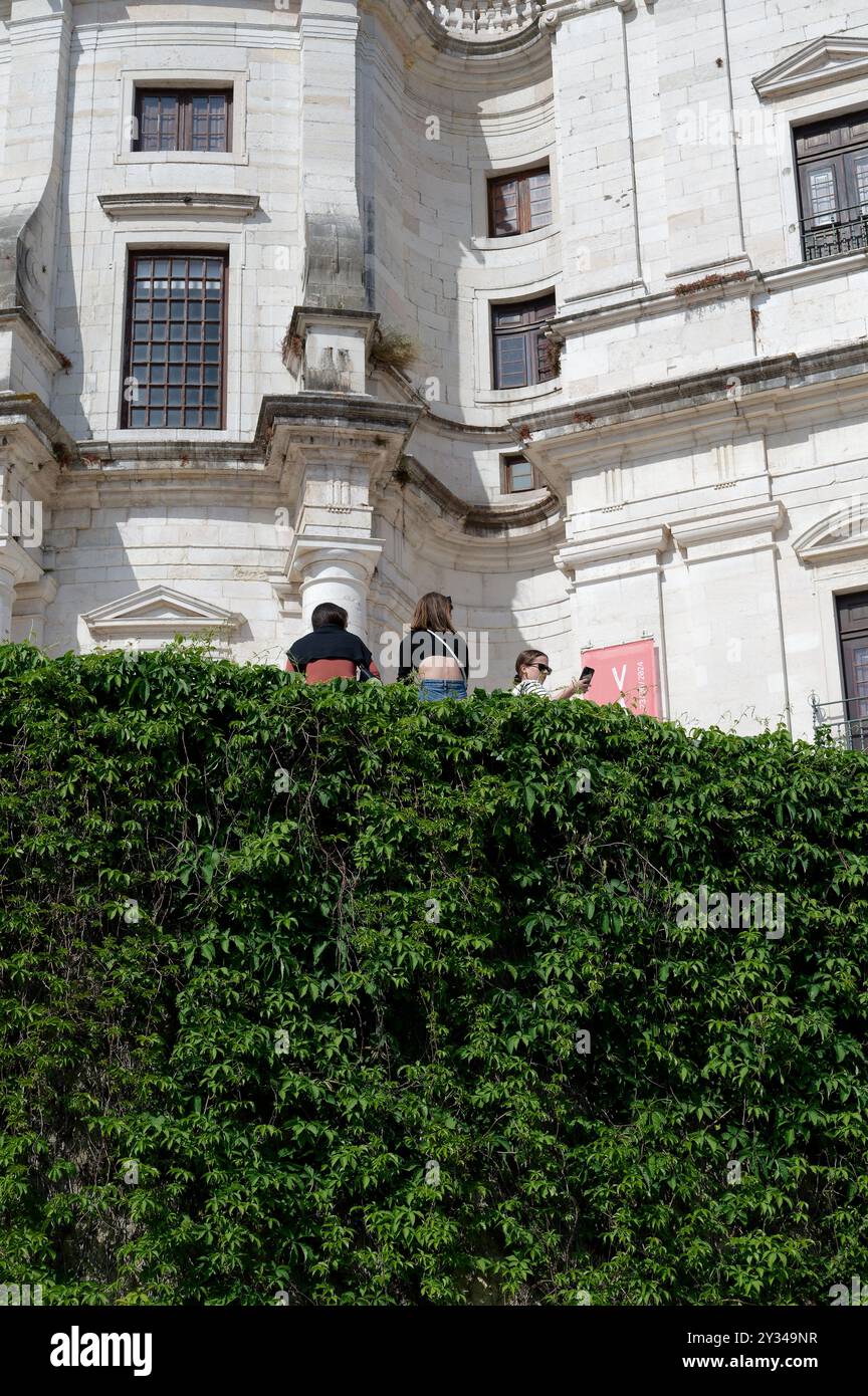 Menschen, die auf einem Vorsprung sitzen, der mit üppigem Grün bedeckt ist, mit der großen Fassade des Panteão Nacional dahinter Stockfoto