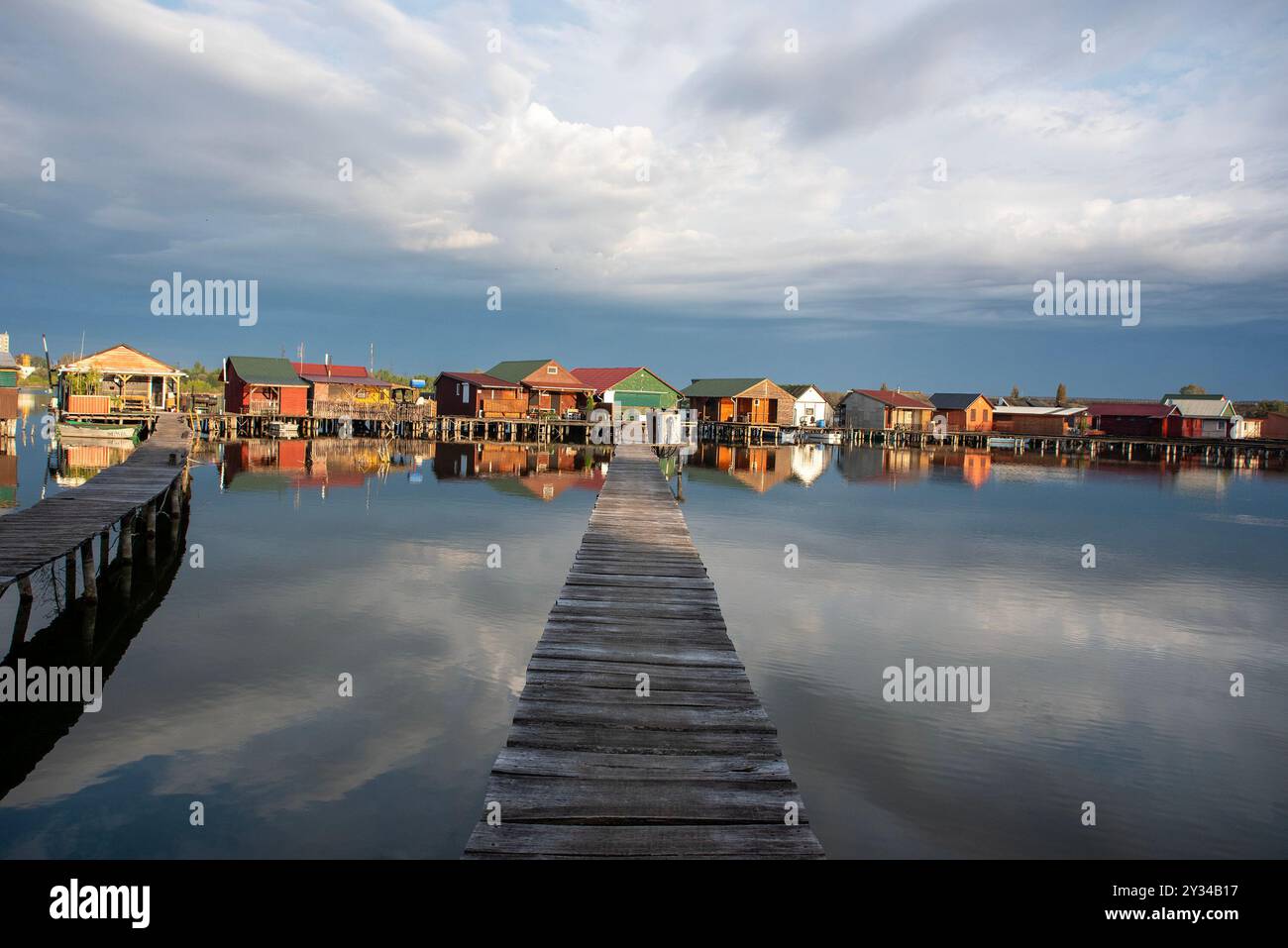 Oroszlany, Ungarn. September 2024. Reflexionen der Gebäude im Wasser und stürmische Wolken am frühen Morgen über dem schwimmenden Dorf Bokodi. Der Bodoki-See ist ein künstlicher See in Oroszlany, Ungarn. Sie wurde 1961 von der Oroszlany Thermal Power Company gegründet. Die Häuser stehen über dem Wasser auf Stelzen. Im Laufe der Jahre wurde der Bokodi-See zu einem beliebten Angelplatz und Ort für Fotografen. (Foto: Krisztian Elek/SOPA Images/SIPA USA) Credit: SIPA USA/Alamy Live News Stockfoto