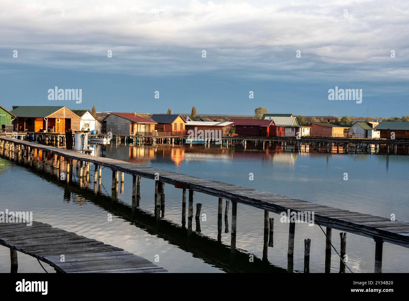 Oroszlany, Ungarn. September 2024. Reflexionen der Gebäude im Wasser und stürmische Wolken am frühen Morgen über dem schwimmenden Dorf Bokodi. Der Bodoki-See ist ein künstlicher See in Oroszlany, Ungarn. Sie wurde 1961 von der Oroszlany Thermal Power Company gegründet. Die Häuser stehen über dem Wasser auf Stelzen. Im Laufe der Jahre wurde der Bokodi-See zu einem beliebten Angelplatz und Ort für Fotografen. (Foto: Krisztian Elek/SOPA Images/SIPA USA) Credit: SIPA USA/Alamy Live News Stockfoto