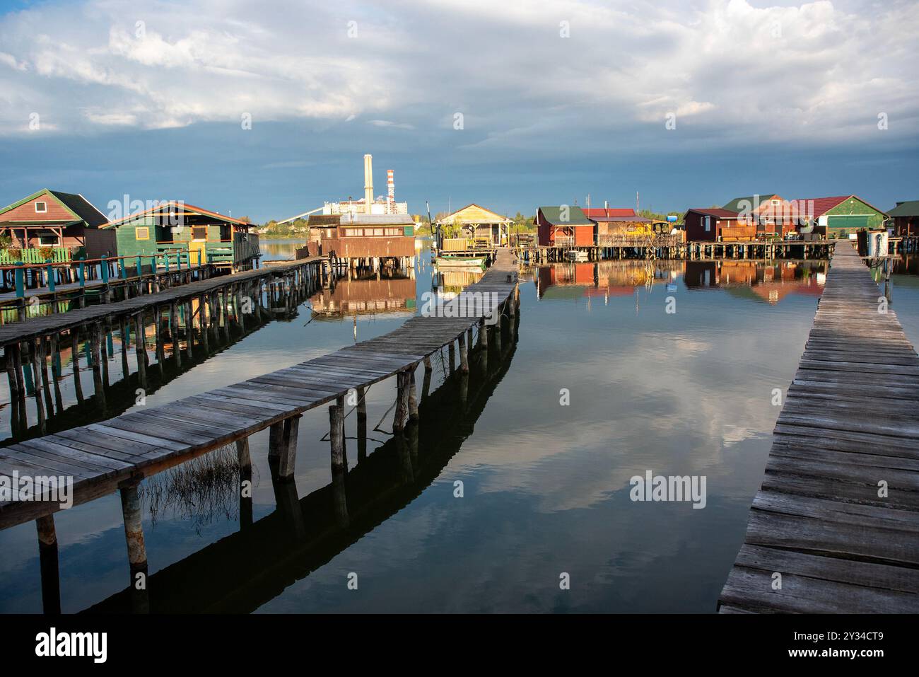 Oroszlany, Ungarn. September 2024. Reflexionen der Gebäude im Wasser und stürmische Wolken am frühen Morgen über dem schwimmenden Dorf Bokodi. Der Bodoki-See ist ein künstlicher See in Oroszlany, Ungarn. Sie wurde 1961 von der Oroszlany Thermal Power Company gegründet. Die Häuser stehen über dem Wasser auf Stelzen. Im Laufe der Jahre wurde der Bokodi-See zu einem beliebten Angelplatz und Ort für Fotografen. Quelle: SOPA Images Limited/Alamy Live News Stockfoto
