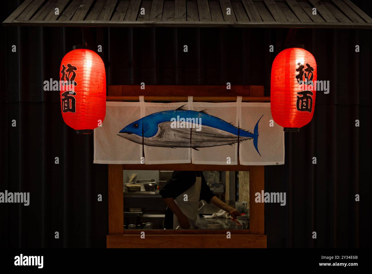 Ein kleiner Ramen-Essensstand mit zwei roten Laternen mit japanischen Schriftzeichen und einem Stoffschild mit einem blauen Thunfisch Stockfoto