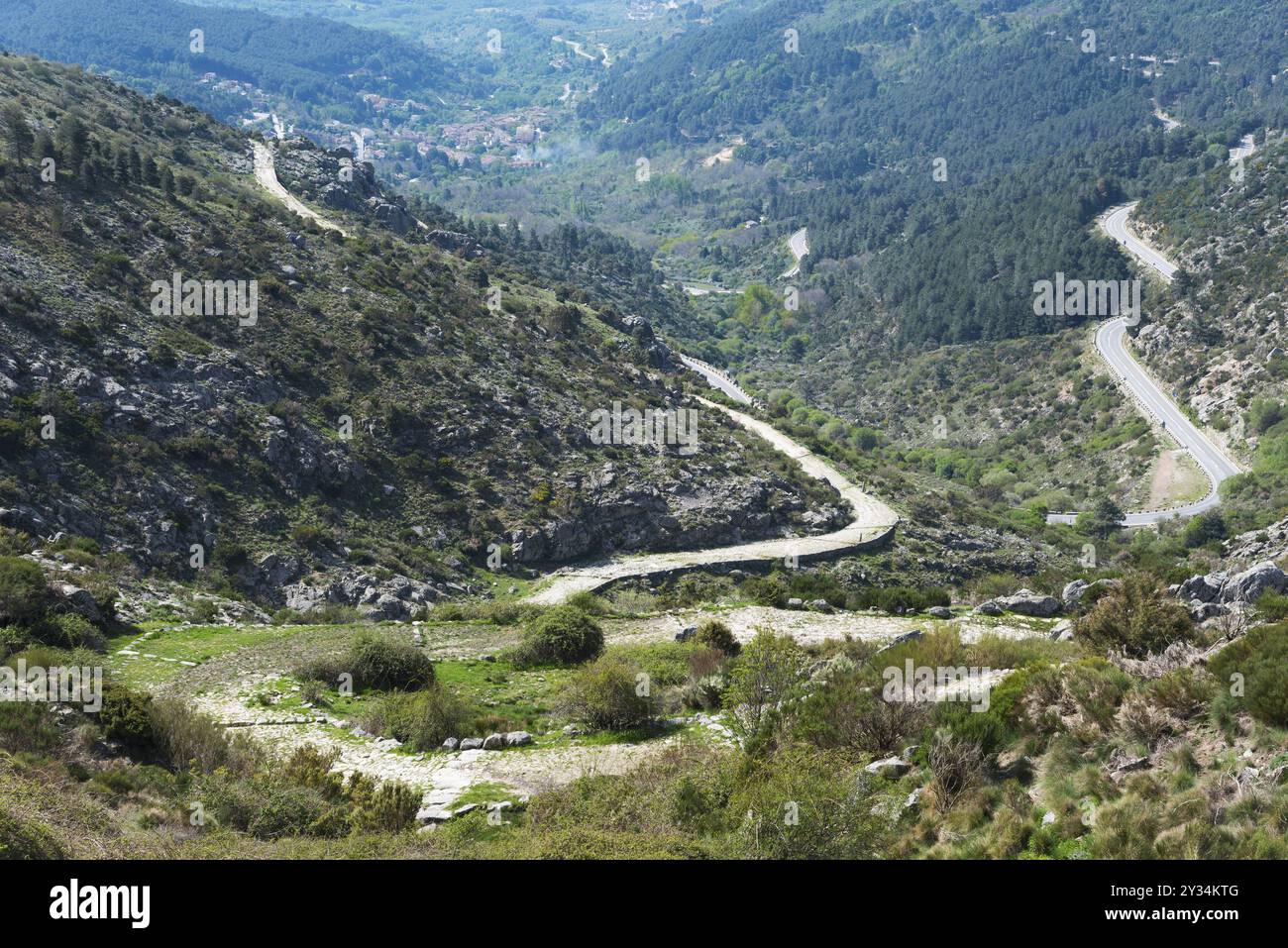 Ein Serpentinenpfad schlängelt sich durch ein grünes Tal mit felsigen Hängen und bewaldeten Hängen, alte Römerstraße, am Puerto del Pico, Sierra de Gredos, Avil Stockfoto