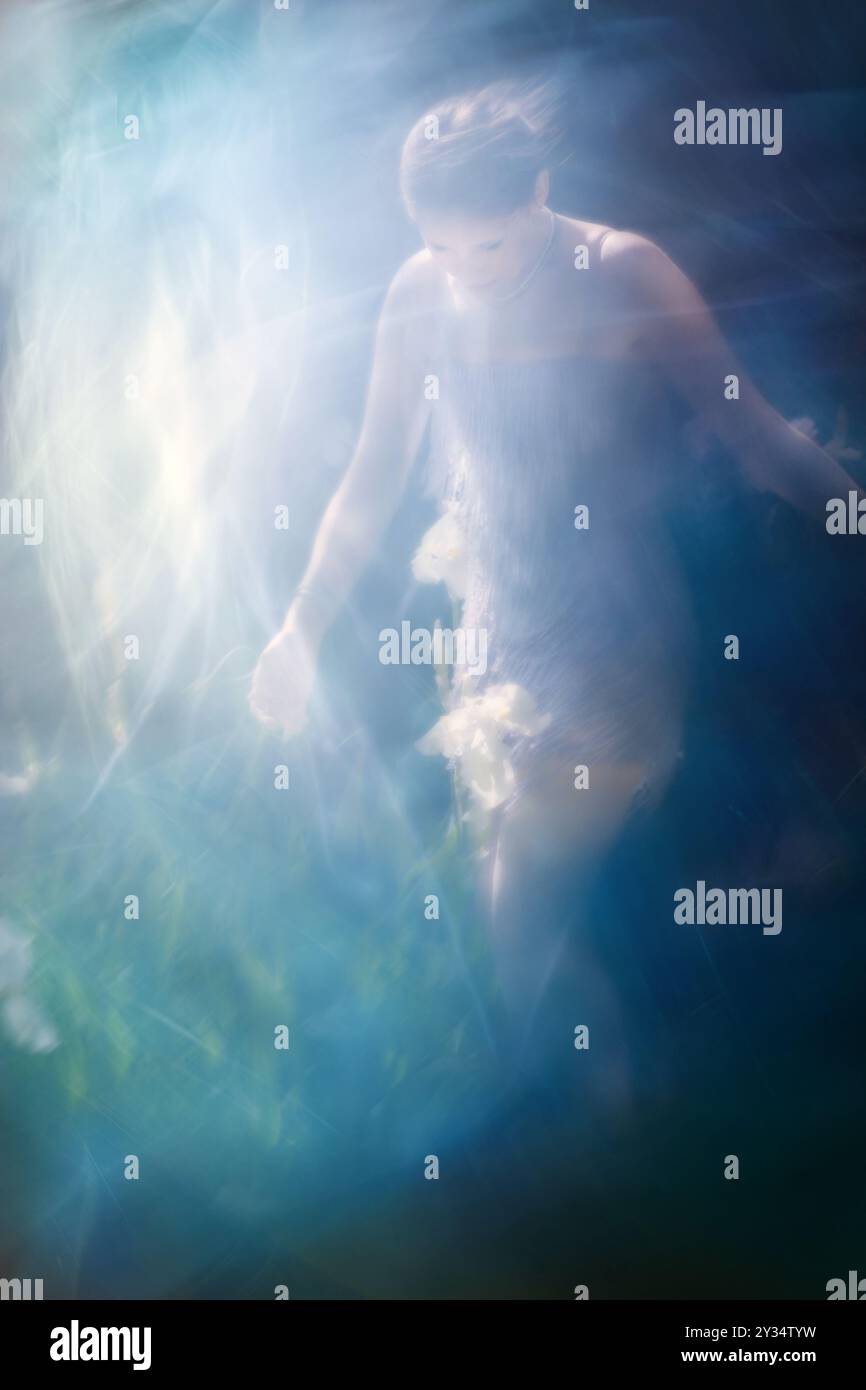 Eine Iris-Blume, die in reinem Licht beleuchtet ist, wird von einer jungen Frau in einem beweglichen Kristallkleid angesprochen. Stockfoto
