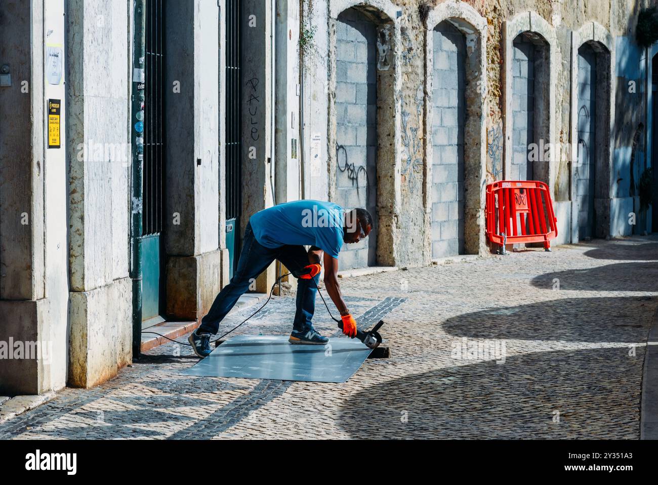 Der Arbeitnehmer konzentriert sich auf das Auftragen einer Schutzbeschichtung auf den Bürgersteig in einer engen Straße von Lissabon Stockfoto