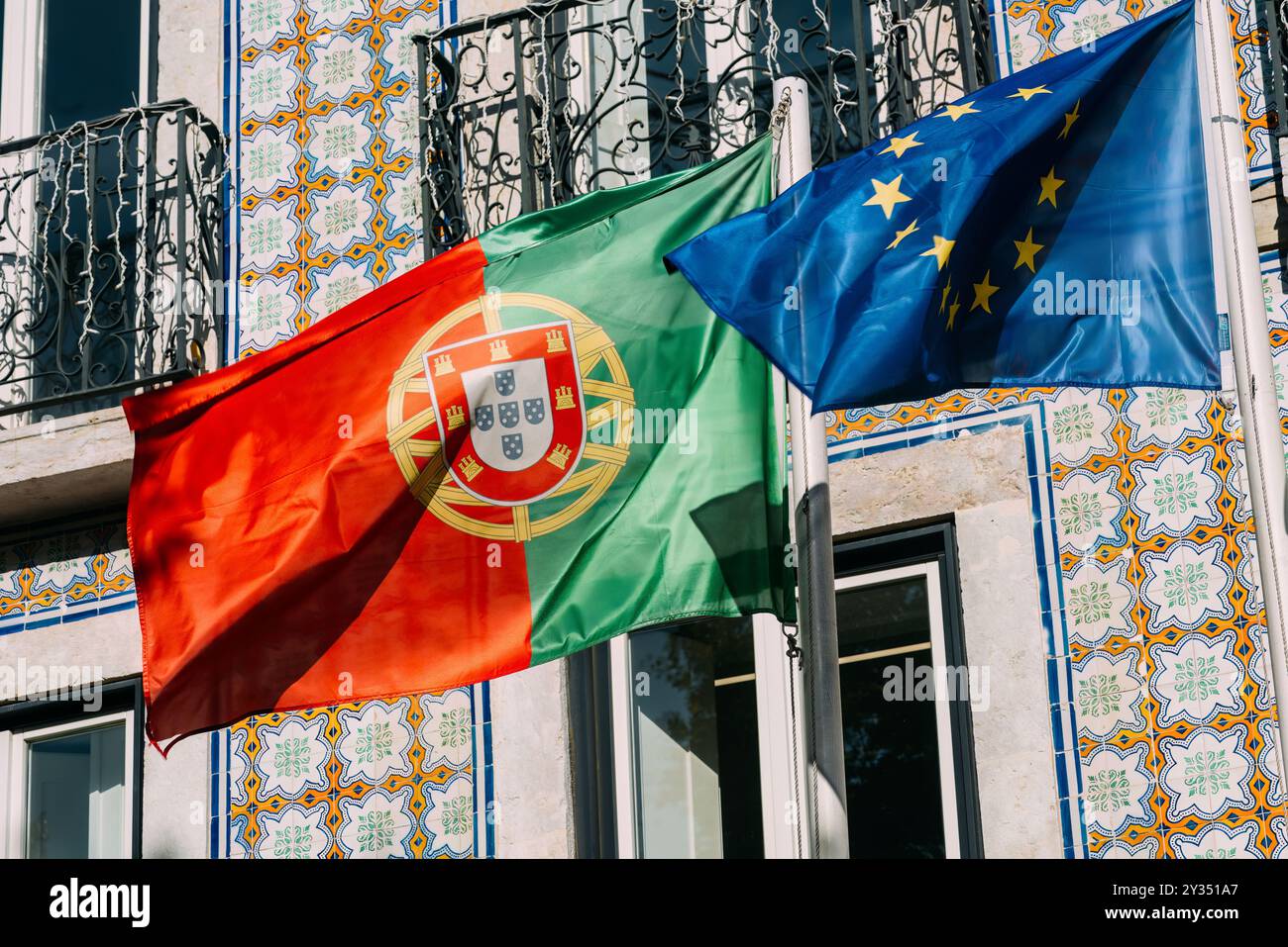 Die belebten portugiesischen und europäischen Flaggen sind gut sichtbar und schweben sanft im Wind vor dem Hintergrund komplizierter Fliesen Stockfoto