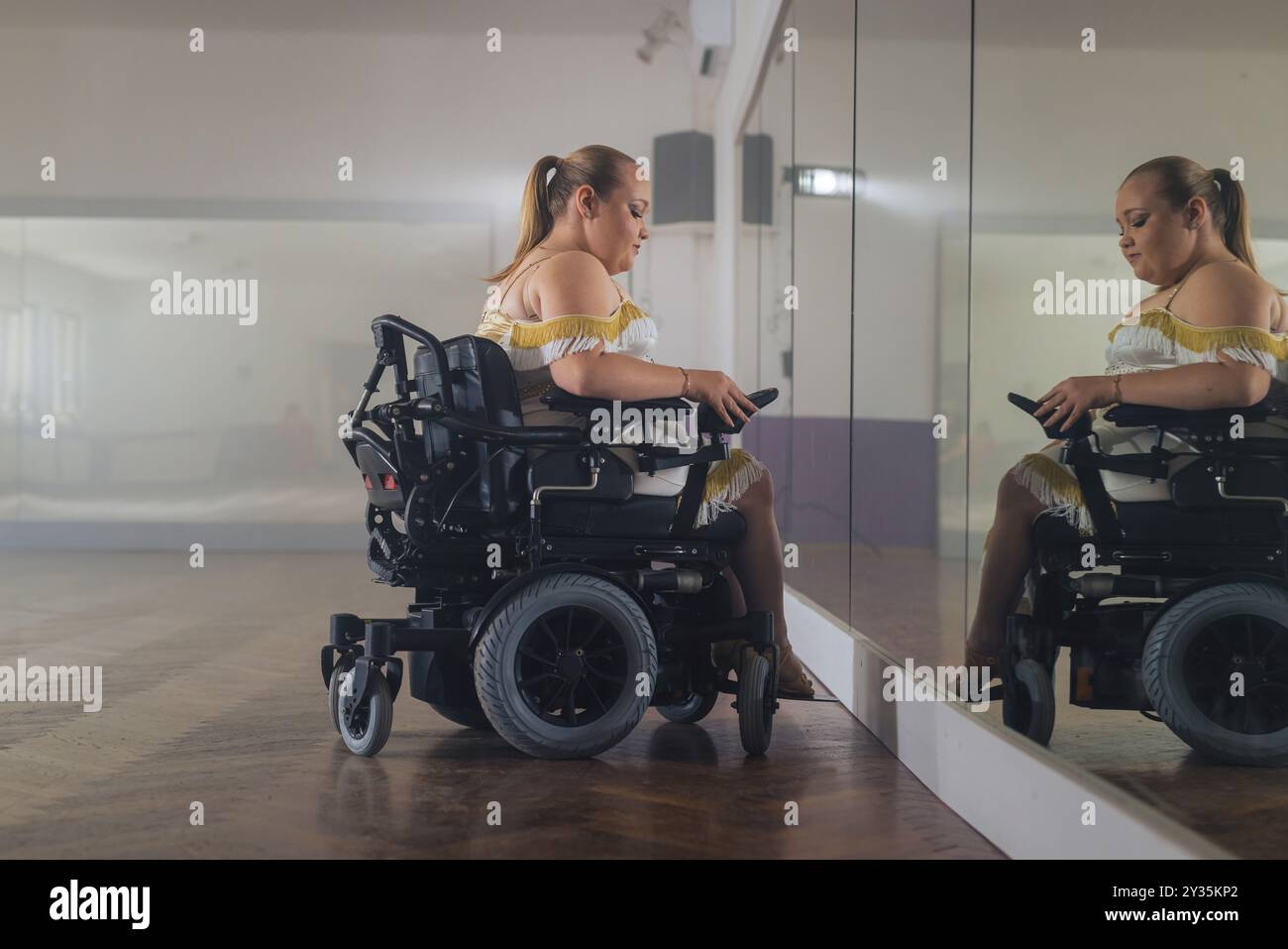 Eine junge Frau, eine Rollstuhltänzerin, die ihren Blick in einem Spiegel in einem Tanzstudio vor der Vorstellung überprüft. Tanz mit Behindertenkonzept. Stockfoto