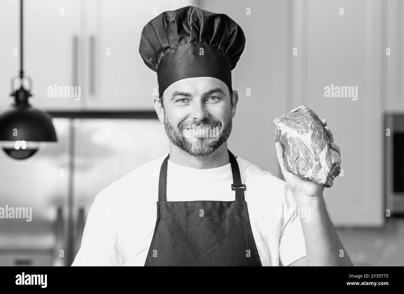 Der Koch-Koch-Koch hat Fleisch-Rindfleisch. Männlicher Koch in Kochuniform mit rohem Rindfleischfilet. Koch-Mann, der rohes Fleisch in der Küche kocht. Stockfoto