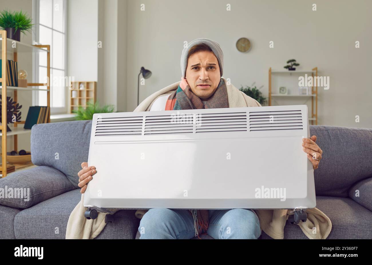 Porträt eines gekühlten Mannes, der in Decke gewickelt ist und eine elektrische Heizung greift Stockfoto Porträt eines gekühlten Mannes, der in Decke gewickelt ist und eine elektrische Heizung greift Stockfoto