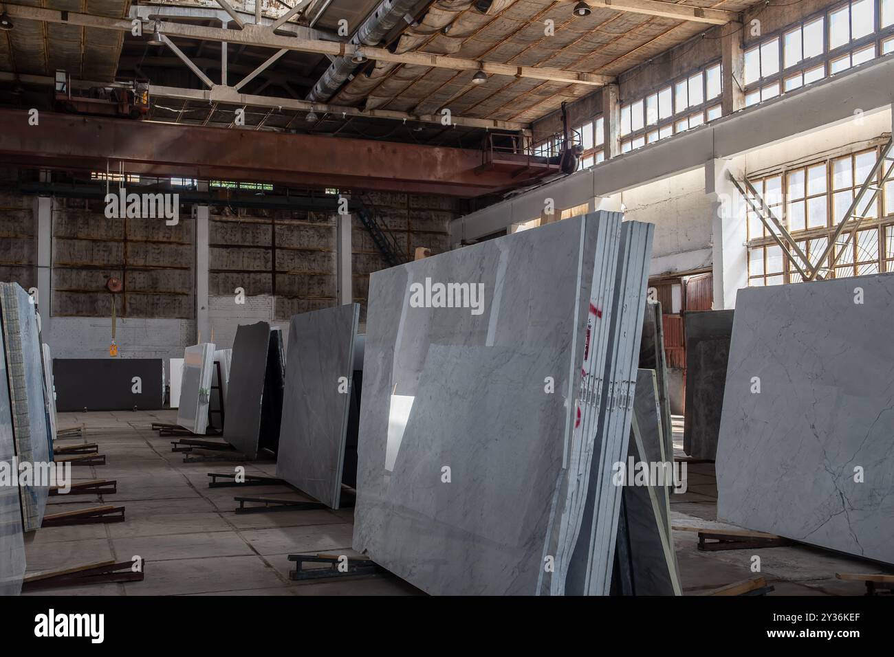 Innenansicht einer Industrieanlage mit großen Fenstern und Natursteinplatten. Weiches natürliches Licht hebt die Texturen hervor Stockfoto