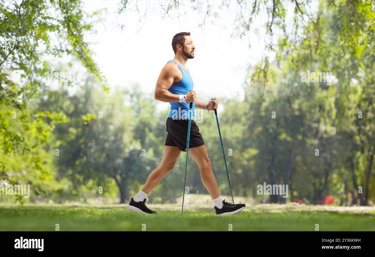 Profilaufnahme eines Mannes, der mit Trekkingstöcken in einem Park läuft Stockfoto