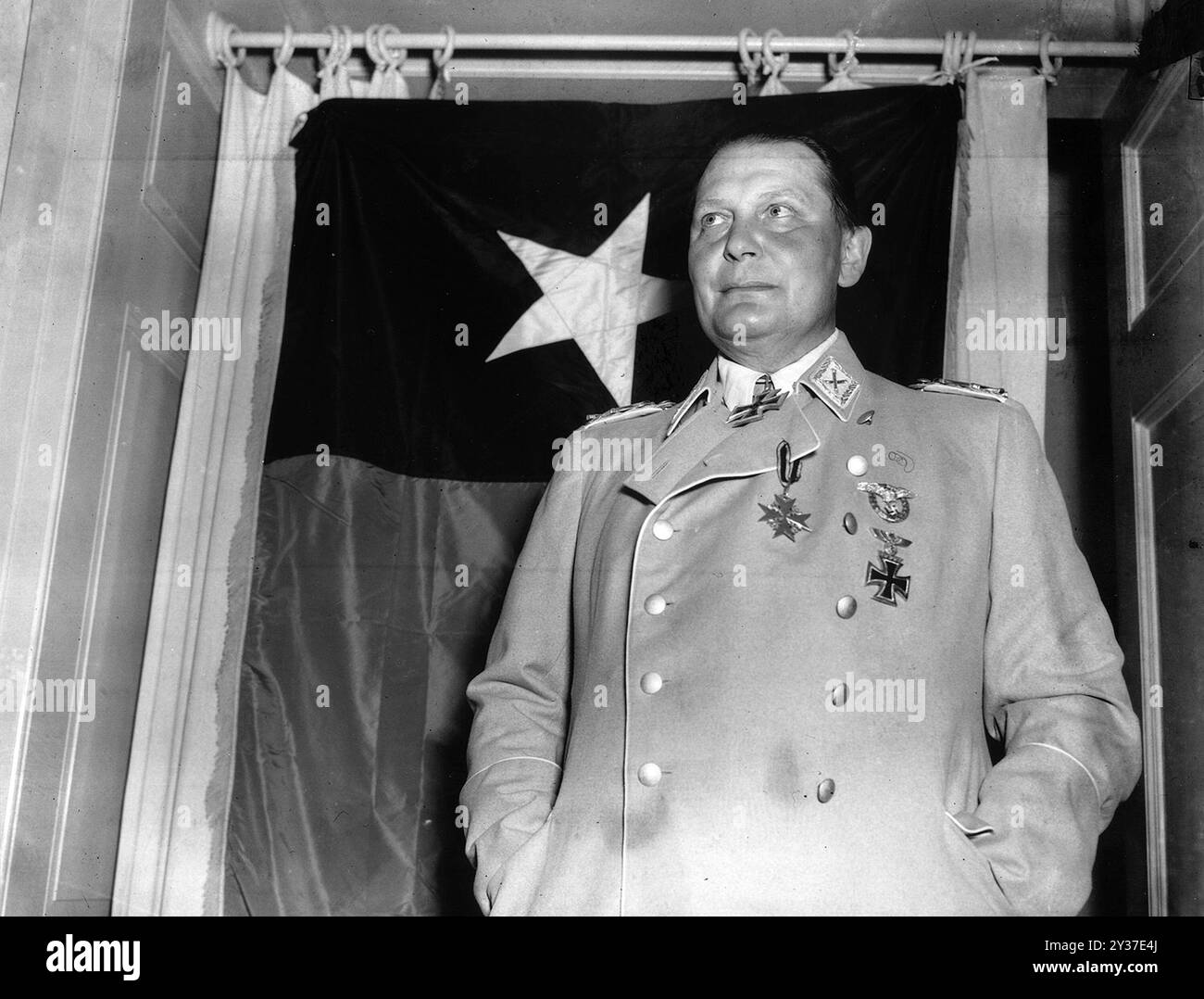 Reichsluftmarschall Hermann Göring posiert vor der Flagge der 36. US-Division auf einer Burg bei Kitzbühel. Göring wurde gefangen genommen, nachdem er von der SS in Berchtesgaden gefangen gehalten wurde. Hitler erließ Anweisungen für seine Hinrichtung. Die Nürnberger Prozesse waren eine Reihe von Prozessen gegen große ns-Militär- und politische Führer. Die Versuche fanden von 1945 bis 1949 statt. Das erste war das Internationale Militärtribunal, das die großen Namen wie Göring, Ribbentrop, Keitel usw. versuchten Es gab 12 Versuche mit Gruppen von Männern, darunter Ärzte, Einsatzgruppen und das militärische Oberkommando. Stockfoto