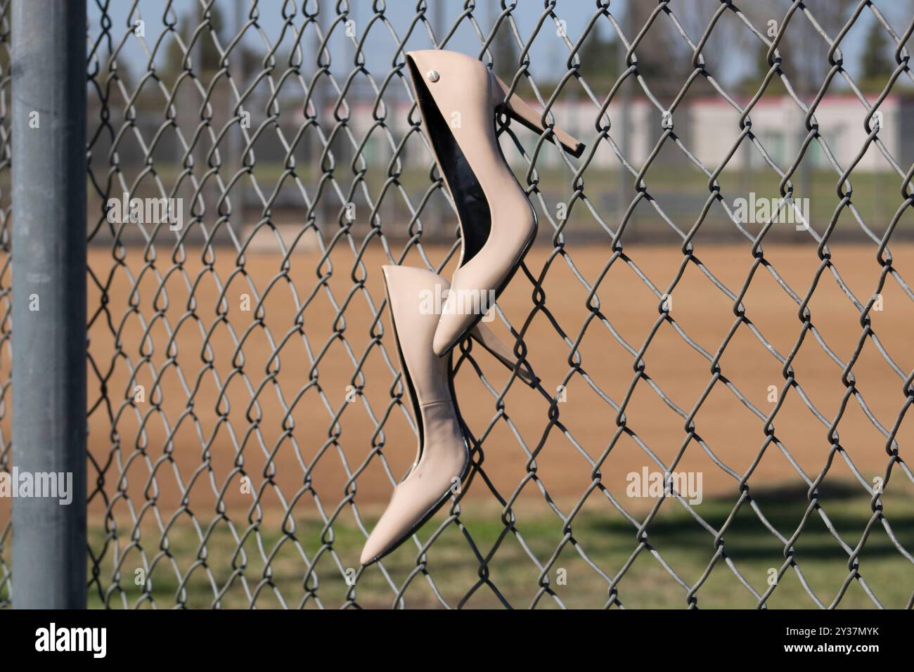 Beige Schuhe mit hohem Absatz, die am Kettenzaun des Baseballfeldes hängen Stockfoto